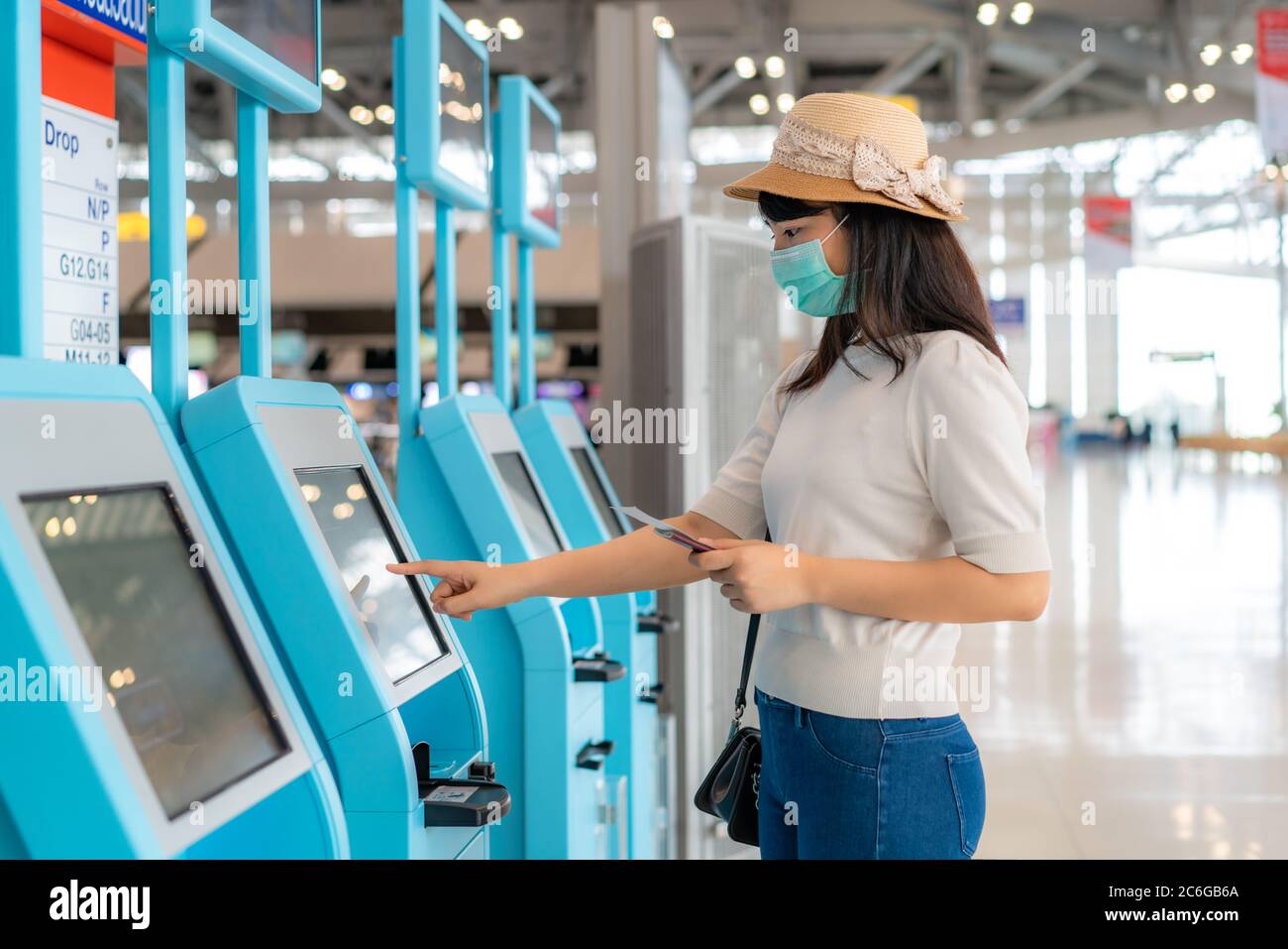 Femme d'Asie qui porte un masque en utilisant un kiosque d'enregistrement automatique dans le terminal de l'aéroport pendant la prévention de la pandémie du coronavirus (COVID-19) lors d'un voyage à l'étranger. Banque D'Images
