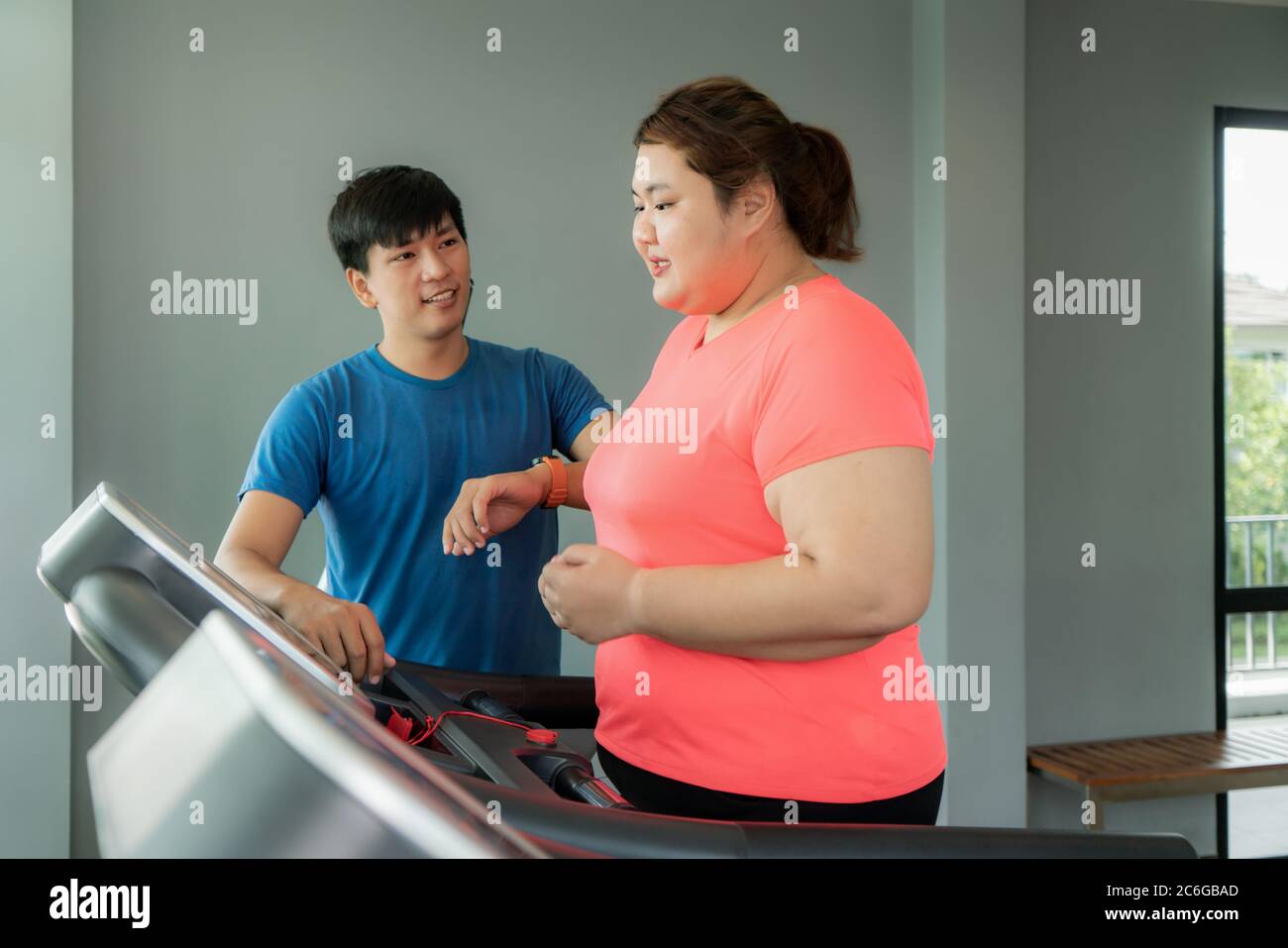 Deux formateurs de l'Asie et de l'embonpoint homme femme l'exercice de formation sur tapis roulant dans une salle de sport, formateur à la recherche heureux son résultat au cours de l'entraînement. Grosses femmes prendre ca Banque D'Images