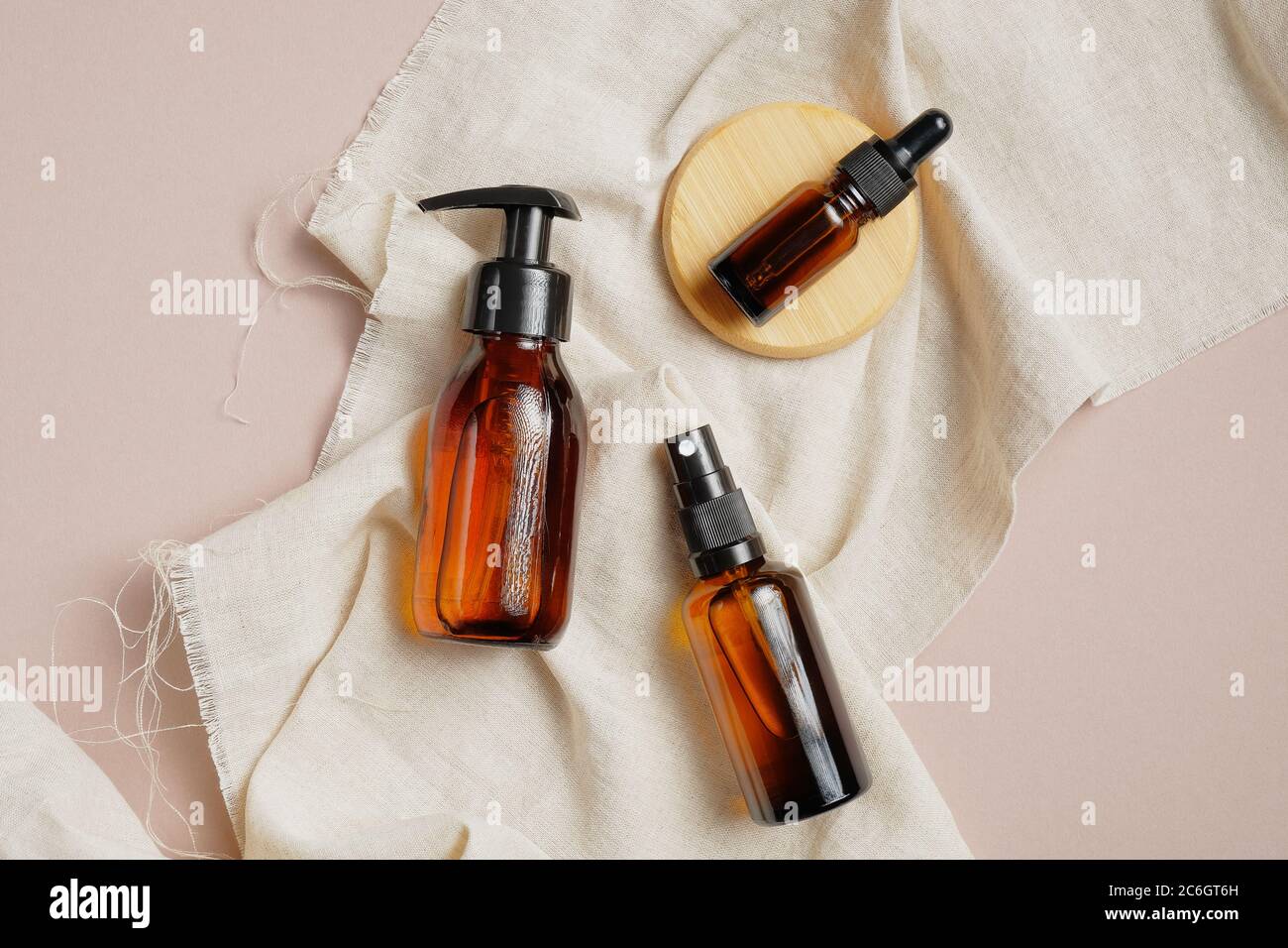 Ensemble d'emballage cosmétique en verre ambré sans étiquette. Distributeur de pompe à pression, flacon compte-gouttes et vaporisateur à plat sur tissu beige. Vue de dessus, au-dessus de la tête. Beaut Banque D'Images