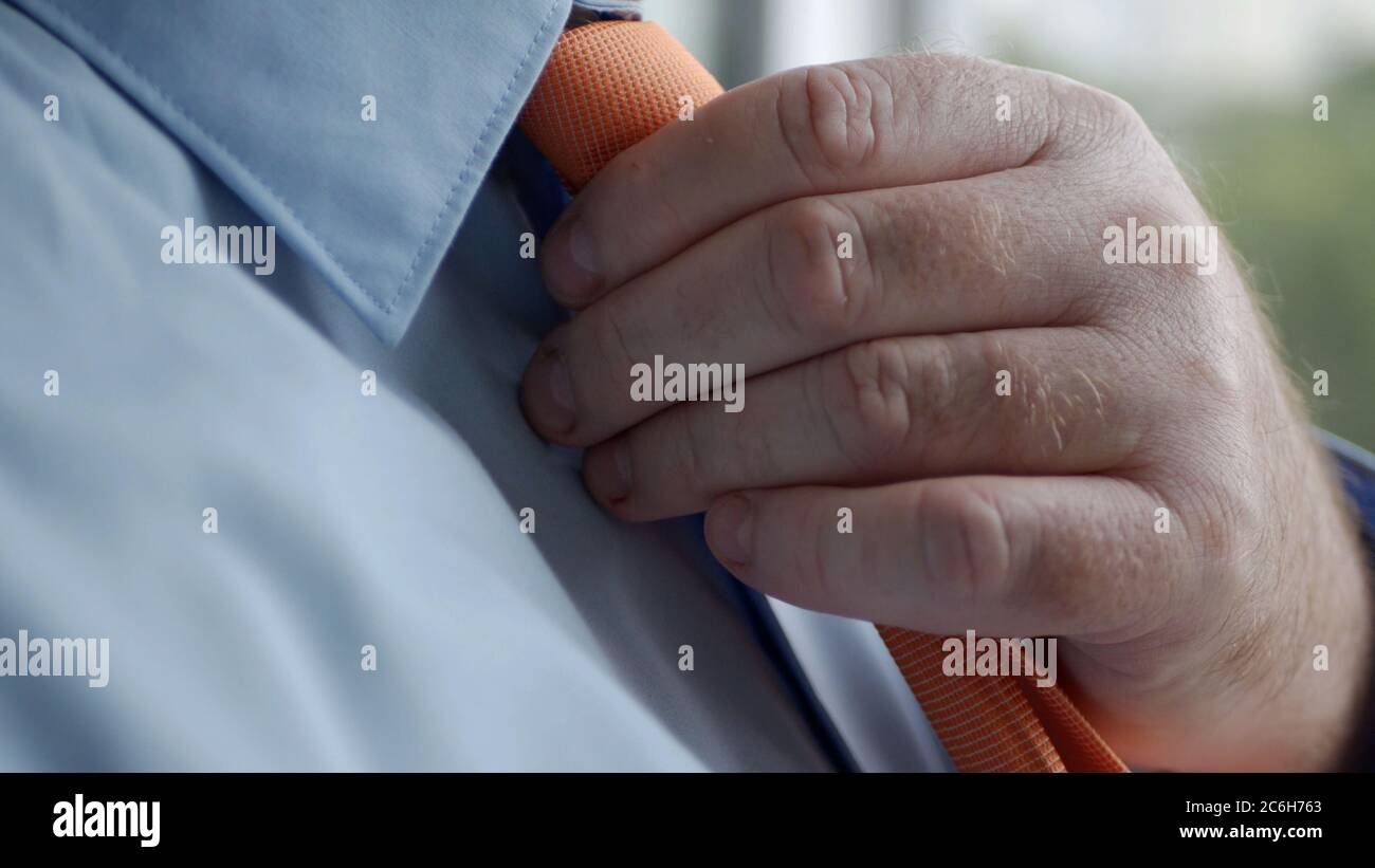 Élégante image homme d'affaires portant une chemise bleue et faisant un nœud à une cravate orange. Banque D'Images
