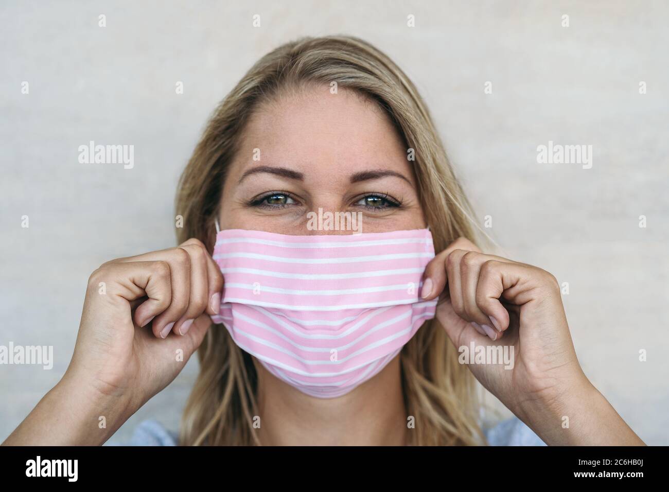Jeune femme portant un masque rose portrait - Blonde femelle utilisant un masque facial protecteur pour prévenir la propagation du virus corona Banque D'Images