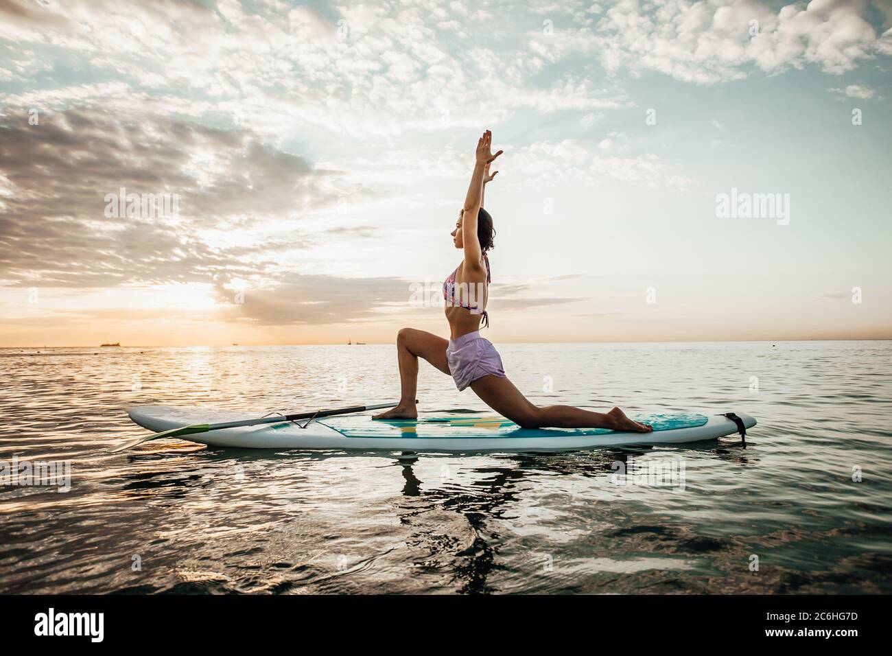 Jeune femme faisant DU YOGA sur un panneau SUP dans le lac au lever du soleil Banque D'Images