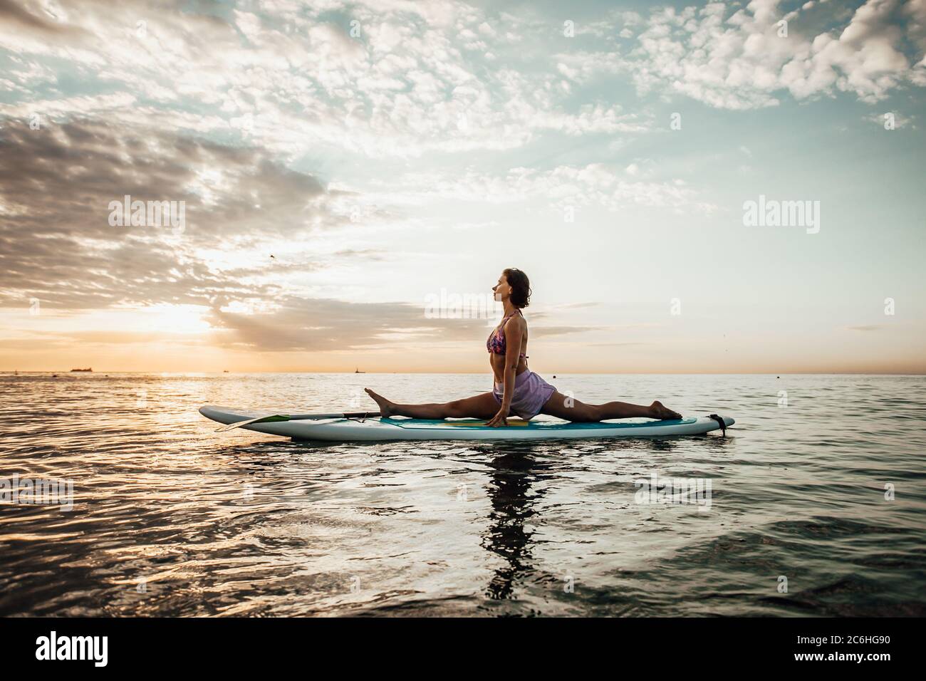 Jeune femme faisant DU YOGA sur un panneau SUP dans le lac au lever du soleil Banque D'Images