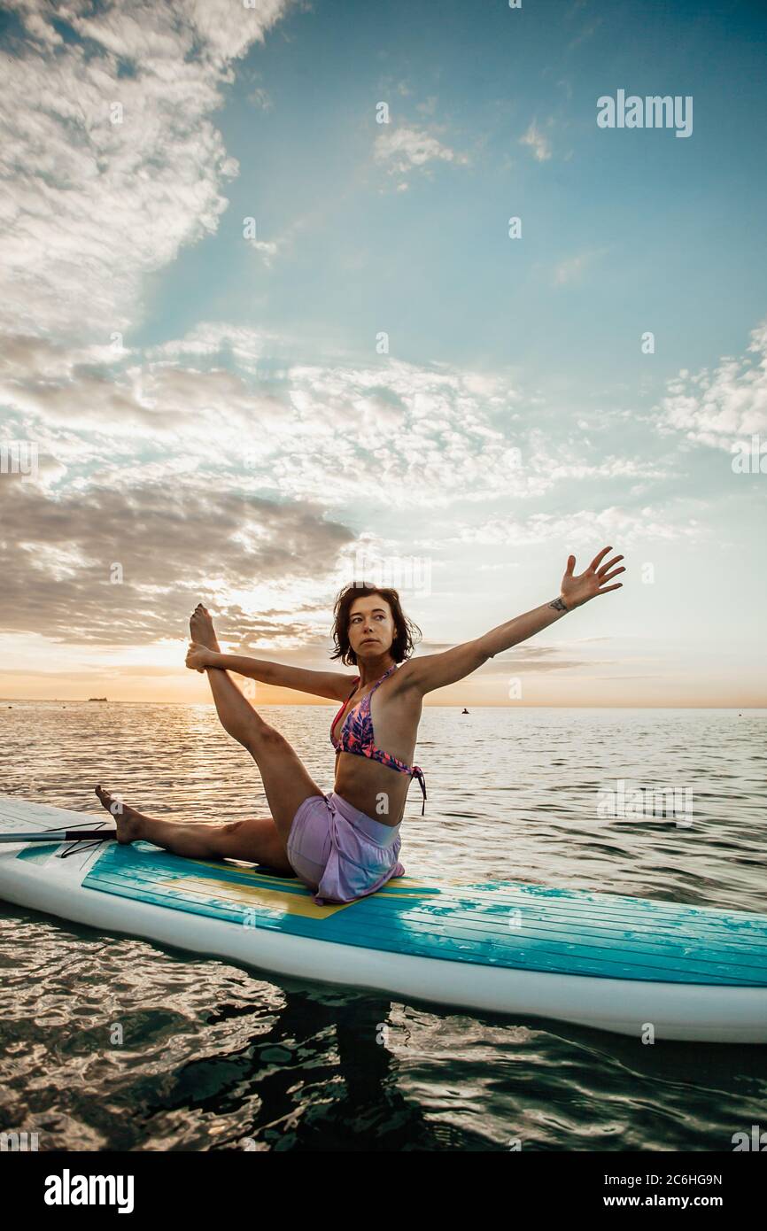 Jeune femme faisant DU YOGA sur un panneau SUP dans le lac au lever du soleil Banque D'Images