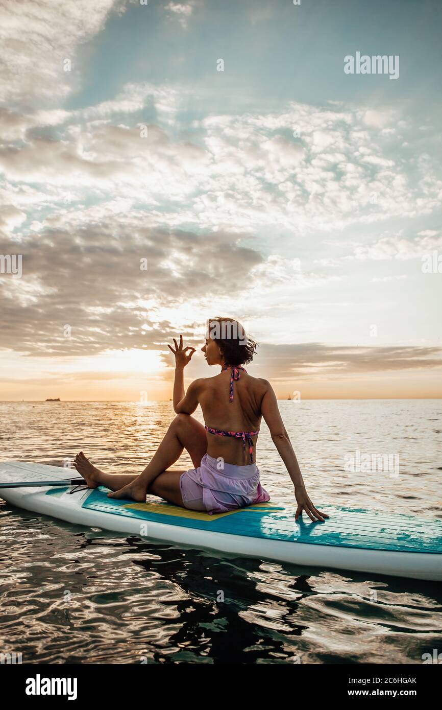 Jeune femme faisant DU YOGA sur un panneau SUP dans le lac au lever du soleil Banque D'Images