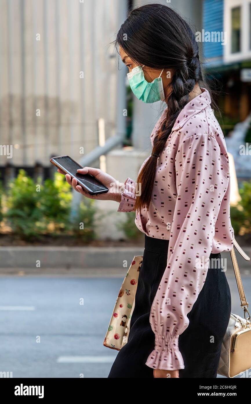 Fille portant un masque facial utilisant un téléphone portable pendant la pandémie de Covid 19, Bangkok, Thaïlande Banque D'Images