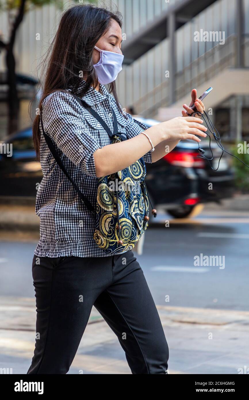 Fille portant un masque facial utilisant un téléphone portable pendant la pandémie de Covid 19, Bangkok, Thaïlande Banque D'Images