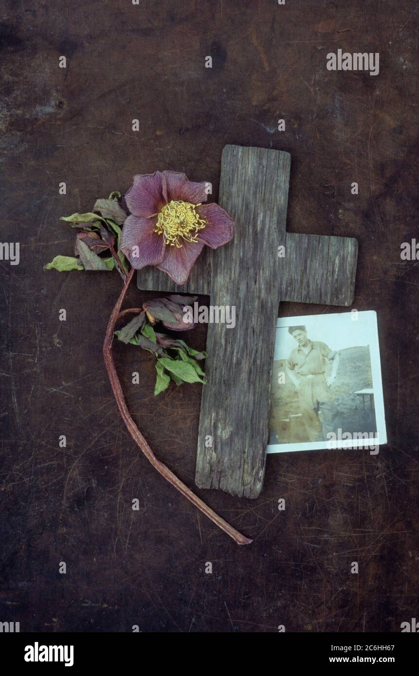 Croix de bois patinée sur métal terni avec rose de Lenton ou Helleborus orientalis décolorés et photo de l'homme des années 1940 dans les vêtements de travail à l'extérieur Banque D'Images