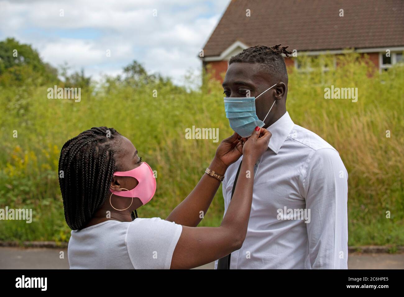 Angleterre, Royaume-Uni. 2020. Portrait d'une femme noire avec un style de cheveux tressé ajustant le masque de son partenaire pendant l'épidémie de Covid-19 Banque D'Images