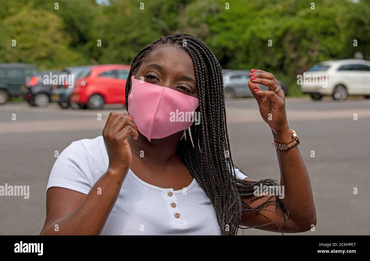 Angleterre, Royaume-Uni. 2020. Portrait d'une femme noire avec un style de cheveux tressé ajustant son masque de couleur rose pendant l'épidémie de Covid-19 Banque D'Images
