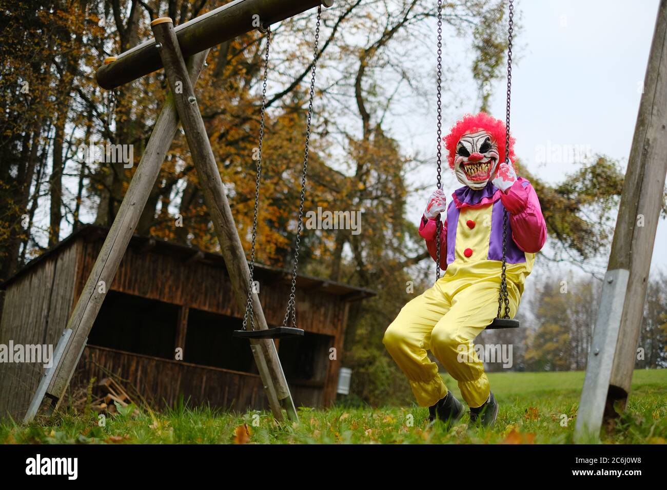 Halloween concept de vacances. Clown effrayant sur un balancement dans la forêt d'automne sur un arrière-plan de hutte ancienne.Horror et la peur. Vacances d'automne. Ambiance halloween Banque D'Images