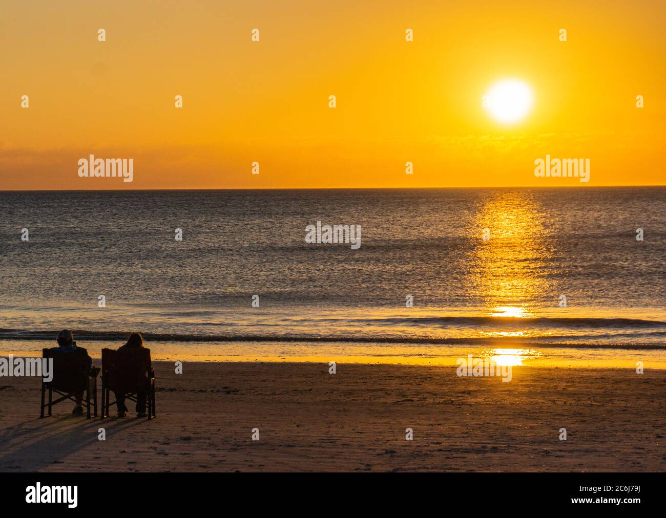 deux personnes assises sur la plage et profitant du coucher du soleil Banque D'Images