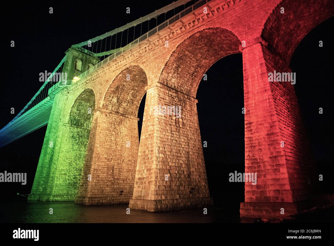 Bangor, Gwynedd, N pays de Galles. Suspension de Menai le pont au-dessus du détroit de Menai est illuminé dans des couleurs arc-en-ciel pour célébrer 72 ans du NHS Banque D'Images