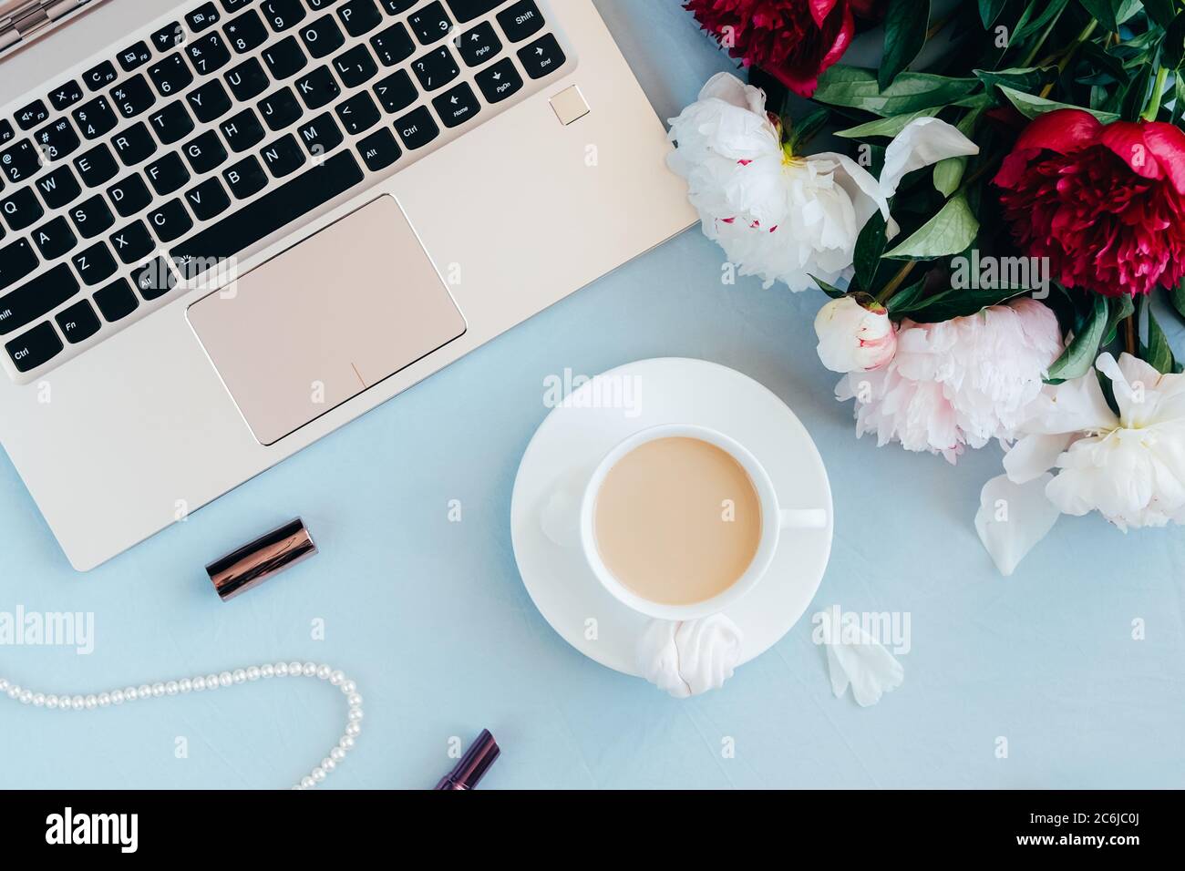Espace de travail féminin avec ordinateur portable, tasse de café, rouge à  lèvres, collier de perles et fleurs de pivoine sur fond bleu. Femme dans le  concept d'affaires. Flat lay, vue de