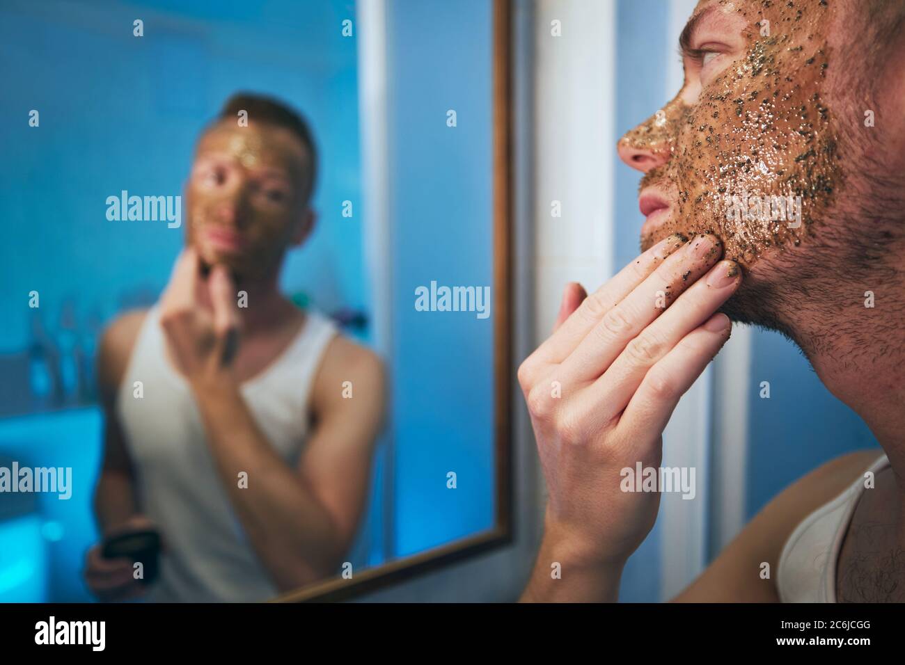 Jeune homme appliquant un masque facial devant le miroir dans la salle de bains à la maison. Thèmes soins de la peau, traitement et beauté pour hommes. Banque D'Images