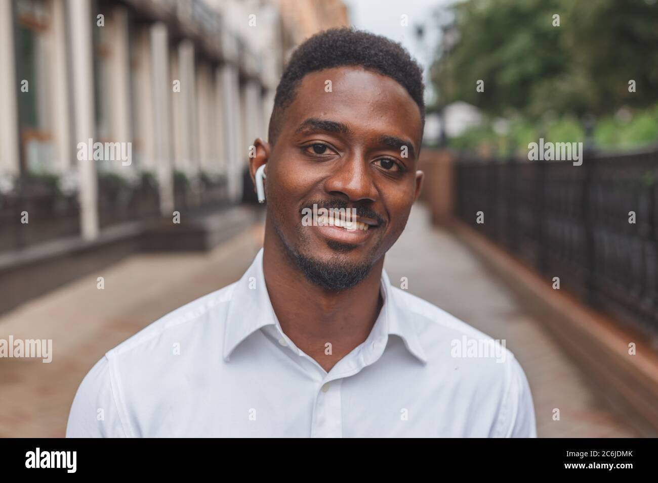 Portrait d'un homme d'affaires noir souriant avec des écouteurs sans fil à l'extérieur Banque D'Images