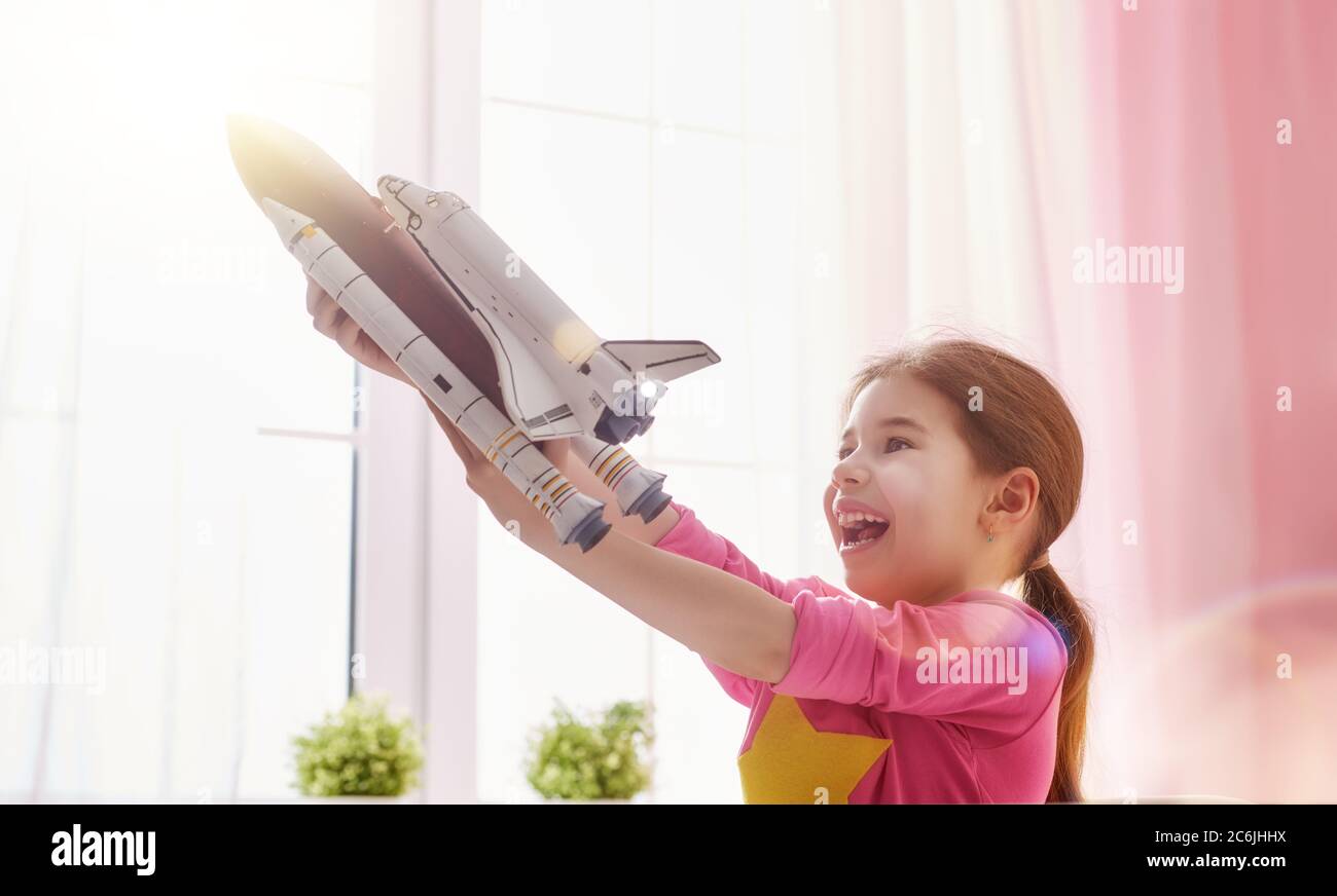 Enfant fille jouant avec la fusée de jouet et rêvant de devenir un joueur d'espace. Portrait d'un enfant drôle près des fenêtres. Banque D'Images