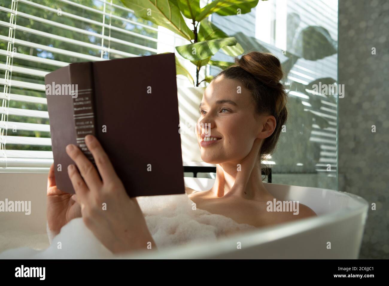 Femme lisant un livre dans une baignoire Banque D'Images