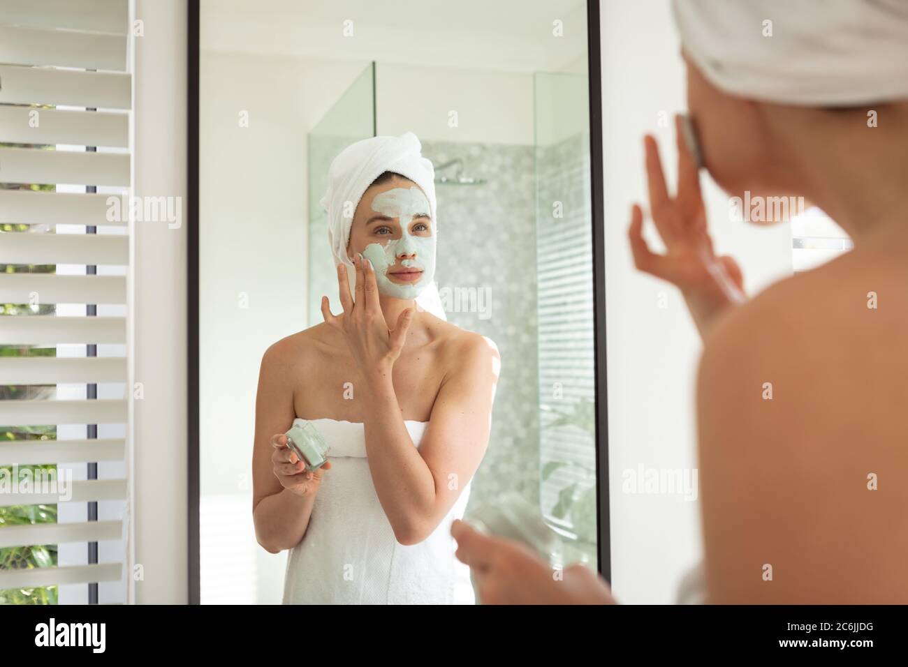 Femme appliquant le paquet de visage en regardant dans le miroir Banque D'Images