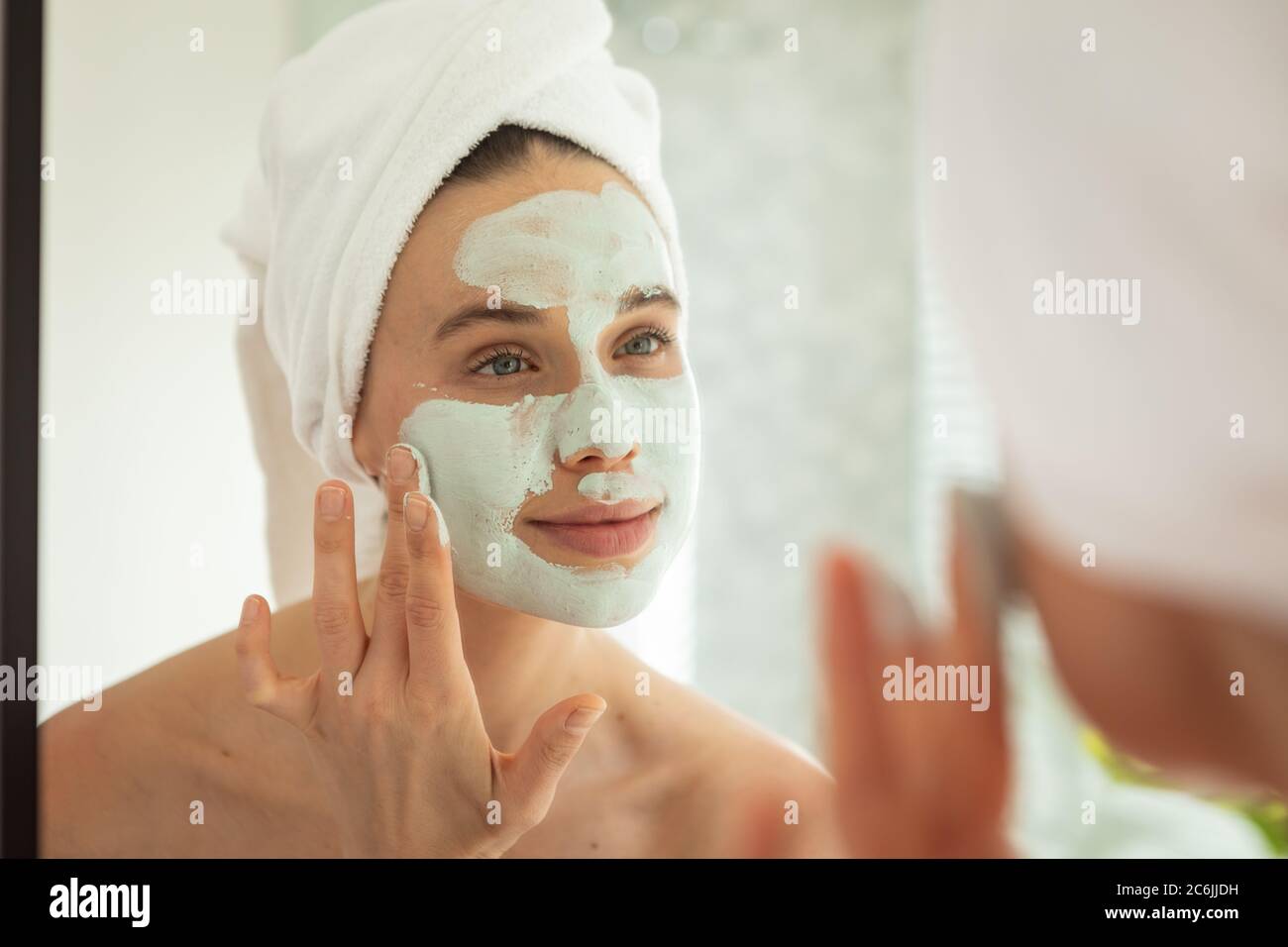 Femme appliquant le paquet de visage en regardant dans le miroir Banque D'Images
