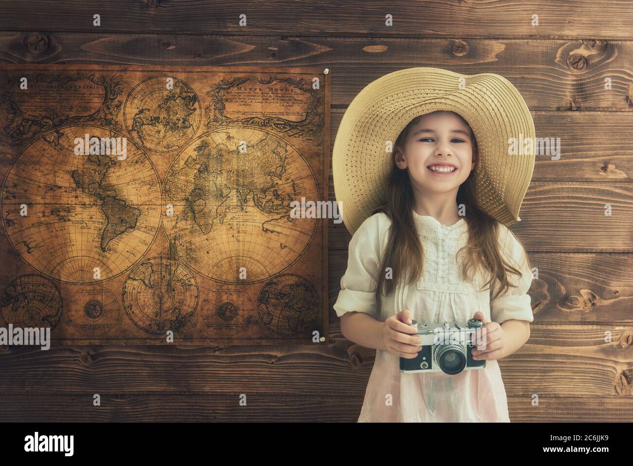 Partez à l'aventure ! Adorable fille avec appareil photo vintage sur un mur en bois et des cartes. Banque D'Images