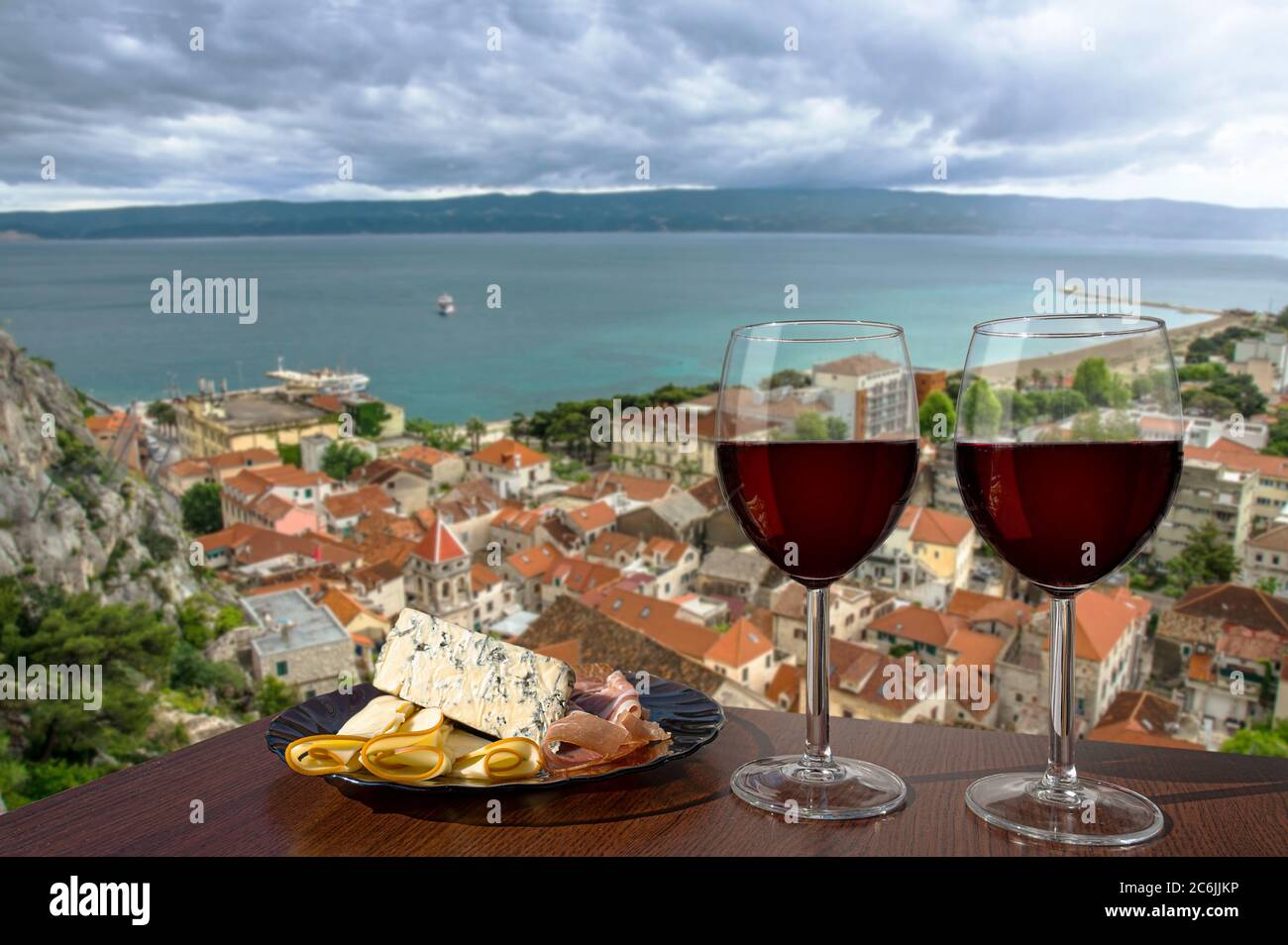 Deux verres de vin rouge avec assortiment de charcuterie avec vue sur la ville croate d'omis avec toits rouges et mer bleue. Verres de vin rouge avec en-cas Banque D'Images