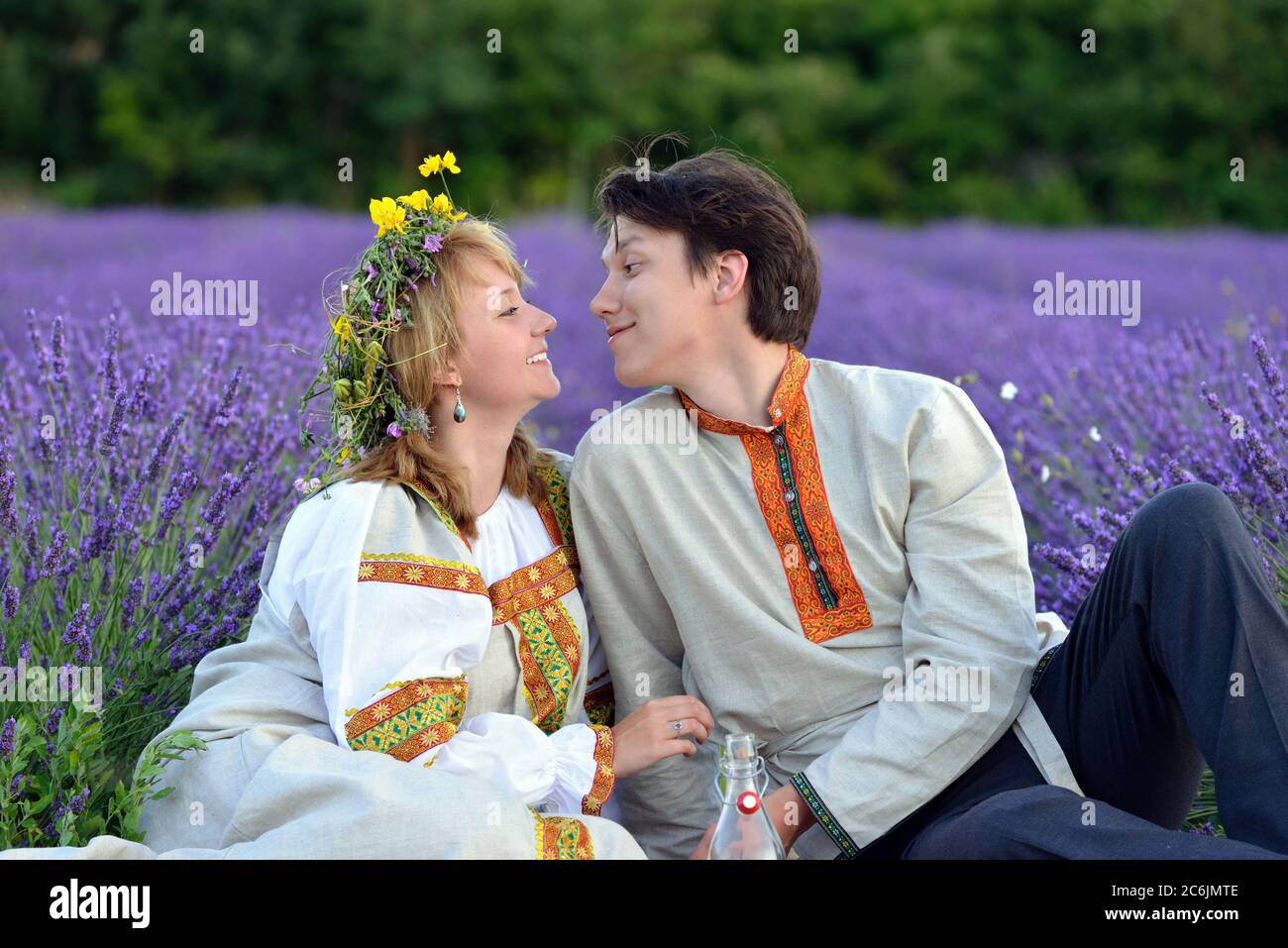 Un jeune couple heureux dans un champ de lavande le soir. Jeune homme et belle fille dans des vêtements russes traditionnels. Banque D'Images