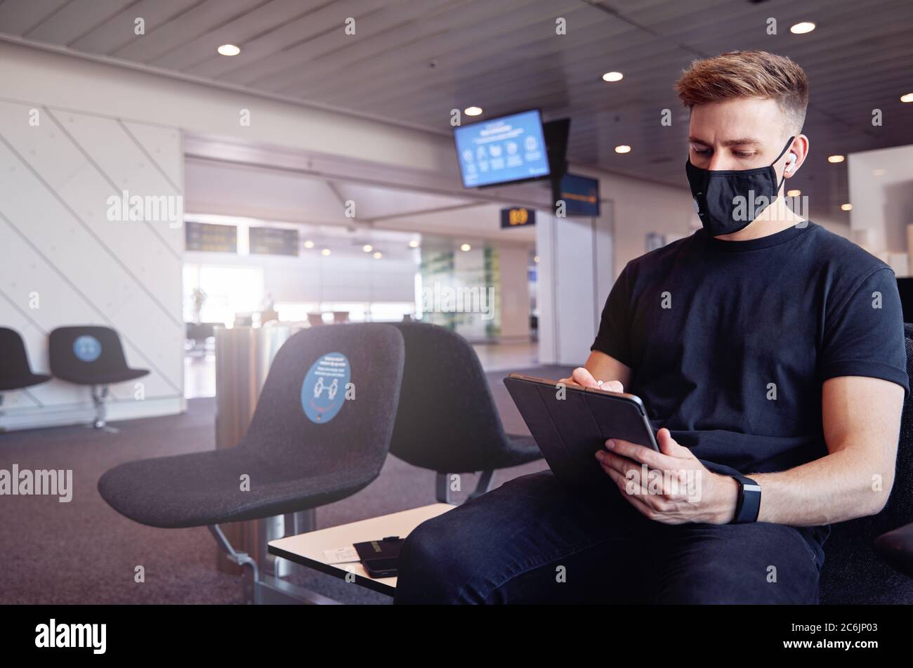 Un homme attendant dans un aéroport vide portant un masque facial de protection utilisant la technologie. Banque D'Images