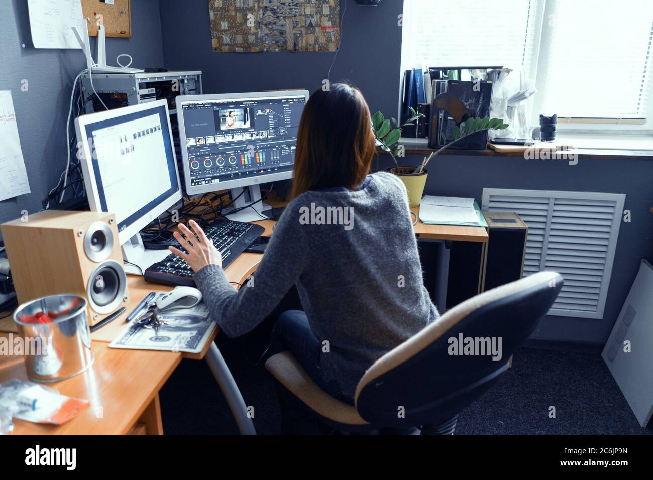 La femme aux cheveux foncés est assise à la table de bureau entourée par Technics et Works dans Video Editor. La fille est passionnée par le travail à l'ordinateur. Le stock de Lipik Banque D'Images