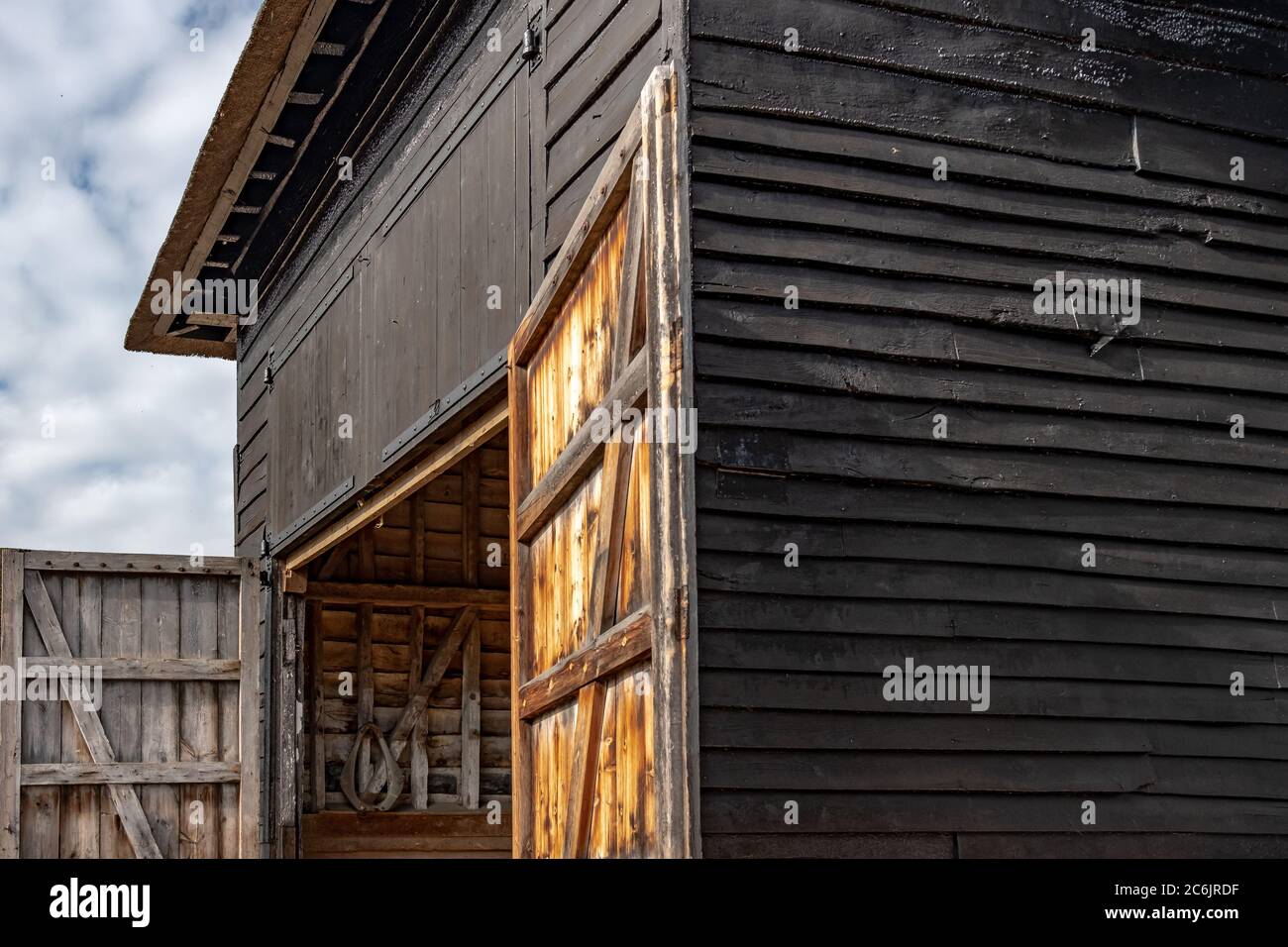 Aspect extérieur d'un grand bâtiment de production et de stockage en bois, illustré par son toit de chaume rénové. Les portes d'entrée sont fermées. Banque D'Images