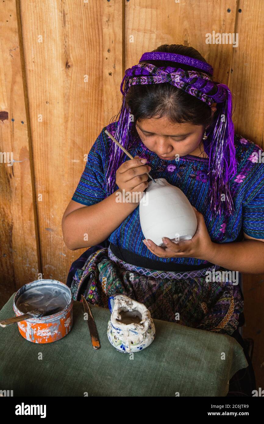 Guatemala, Solola, San Antonio Palopo, UNE jeune femme maya, portant une robe traditionnelle typique, peint des dessins sur la poterie dans un atelier. Banque D'Images