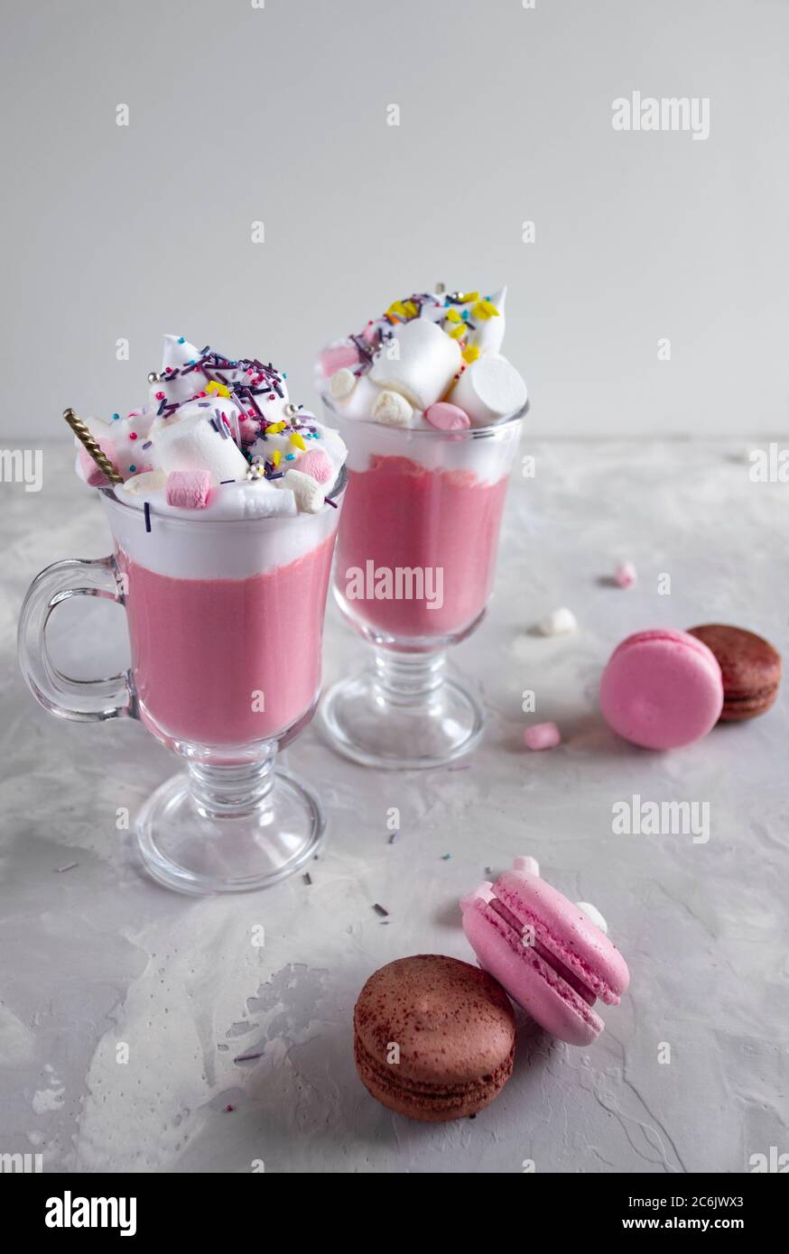 Chocolat chaud rose avec crème fouettée et bonbons guimauve dans 2 tasses en verre, macarons français doux pastel sur fond gris. Copier l'espace Banque D'Images
