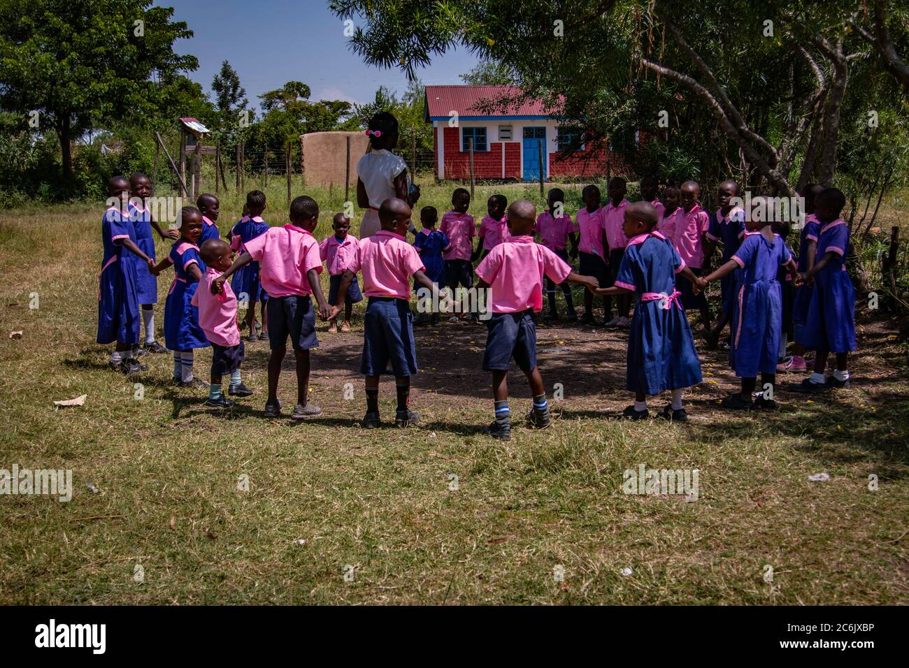 Les enfants des écoles tiennent les mains et forment un cercle autour de leur professeur lorsqu'ils jouent à l'ombre pour échapper au soleil africain Banque D'Images
