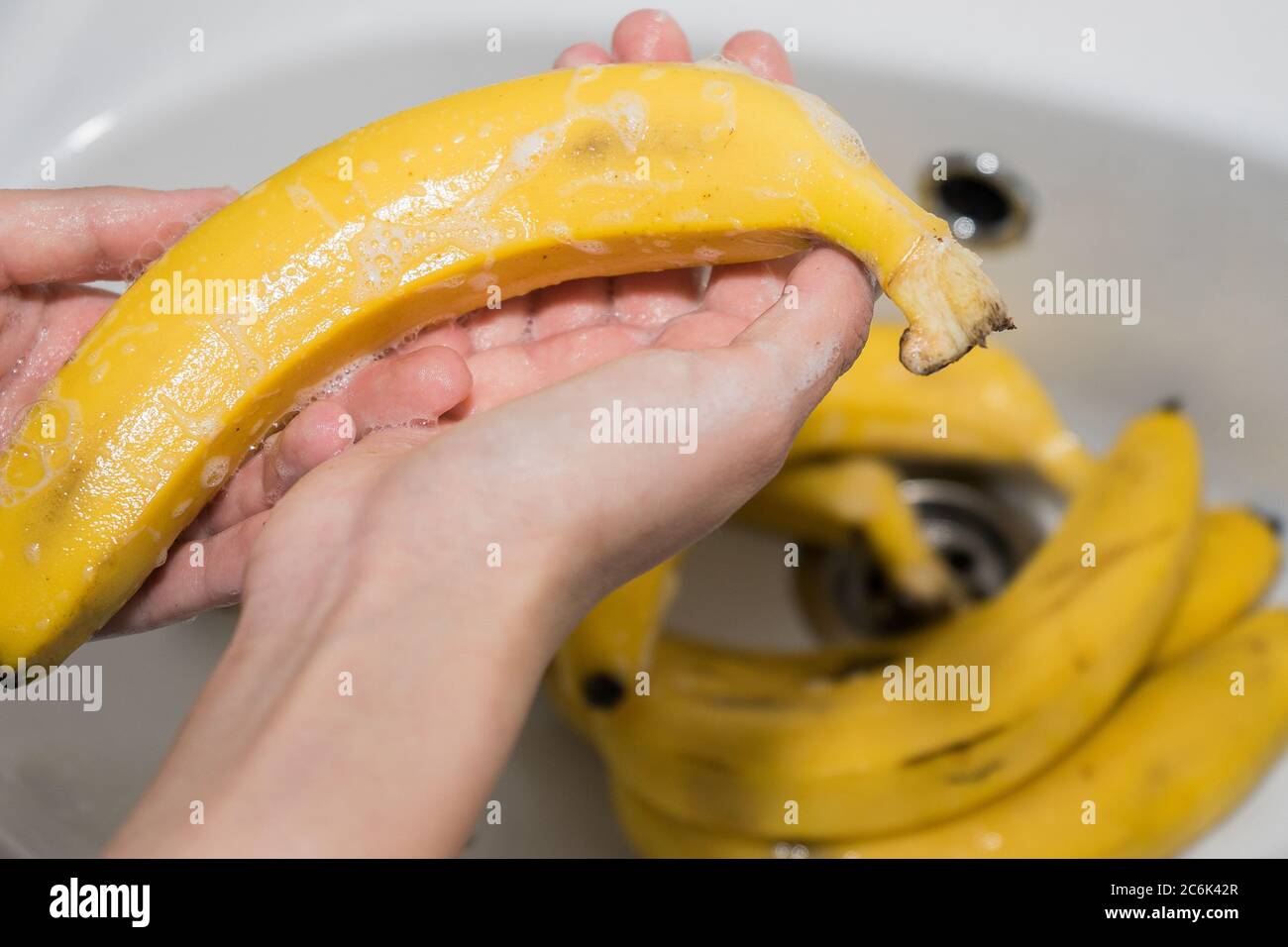 La fille lave les bananes avec du savon. Mains et bananes savonnelles dans l'évier. Banque D'Images