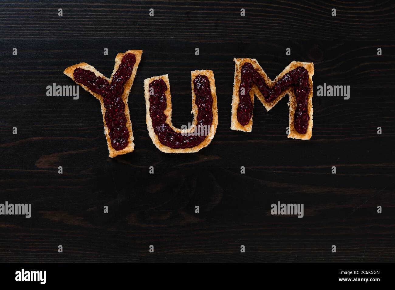 Pain blanc grillé coupé en lettres pour épeler le mot YUM avec de la confiture de framboise Banque D'Images