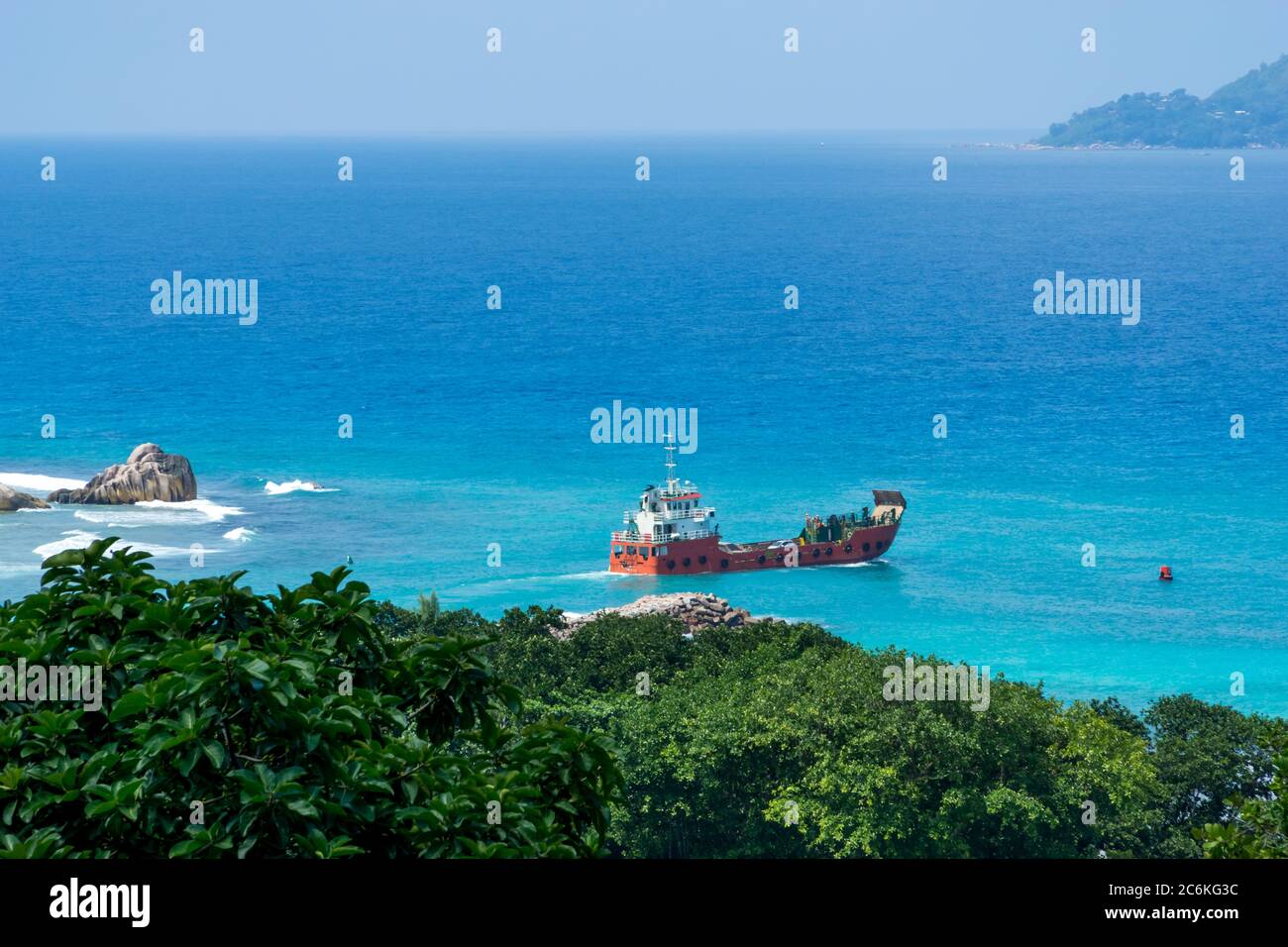 Vue panoramique sur les célèbres rochers de granit dans la mer bleue à la Digue, Seychelles. Navire de cargaison orange allant à l'île de Praslin Banque D'Images