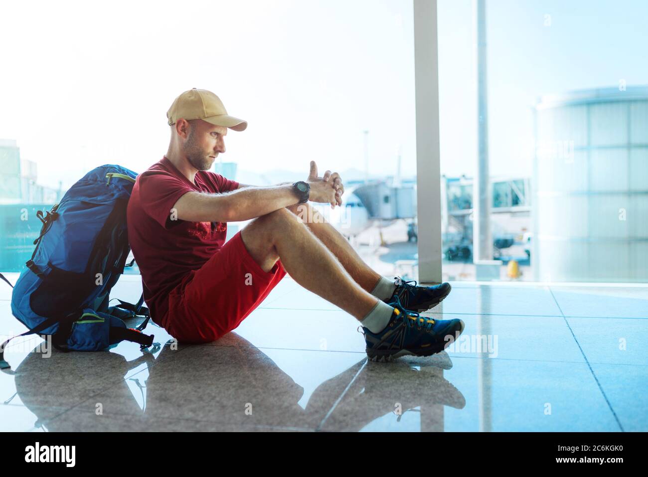 Seul voyageur routard assis au niveau du terminal de l'aéroport et attendant l'embarquement à l'avion qui s'est préparé pour un vol derrière une fenêtre Banque D'Images