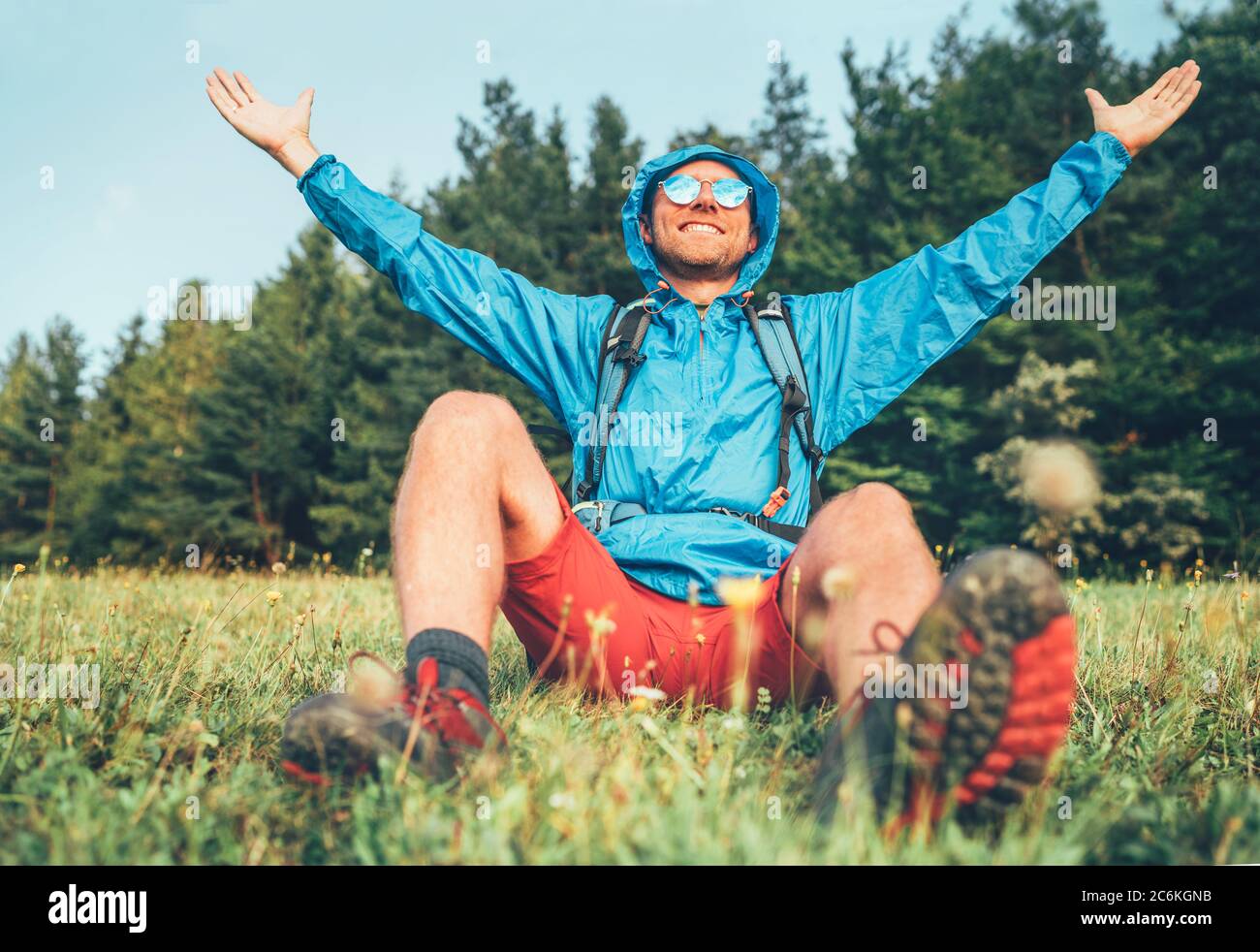 Backpacker homme a une pause de repos appréciant paysage de montagne large ouvert et bras levés. Il porte un poncho bleu imperméable et des lunettes de soleil bleues. Actif Banque D'Images