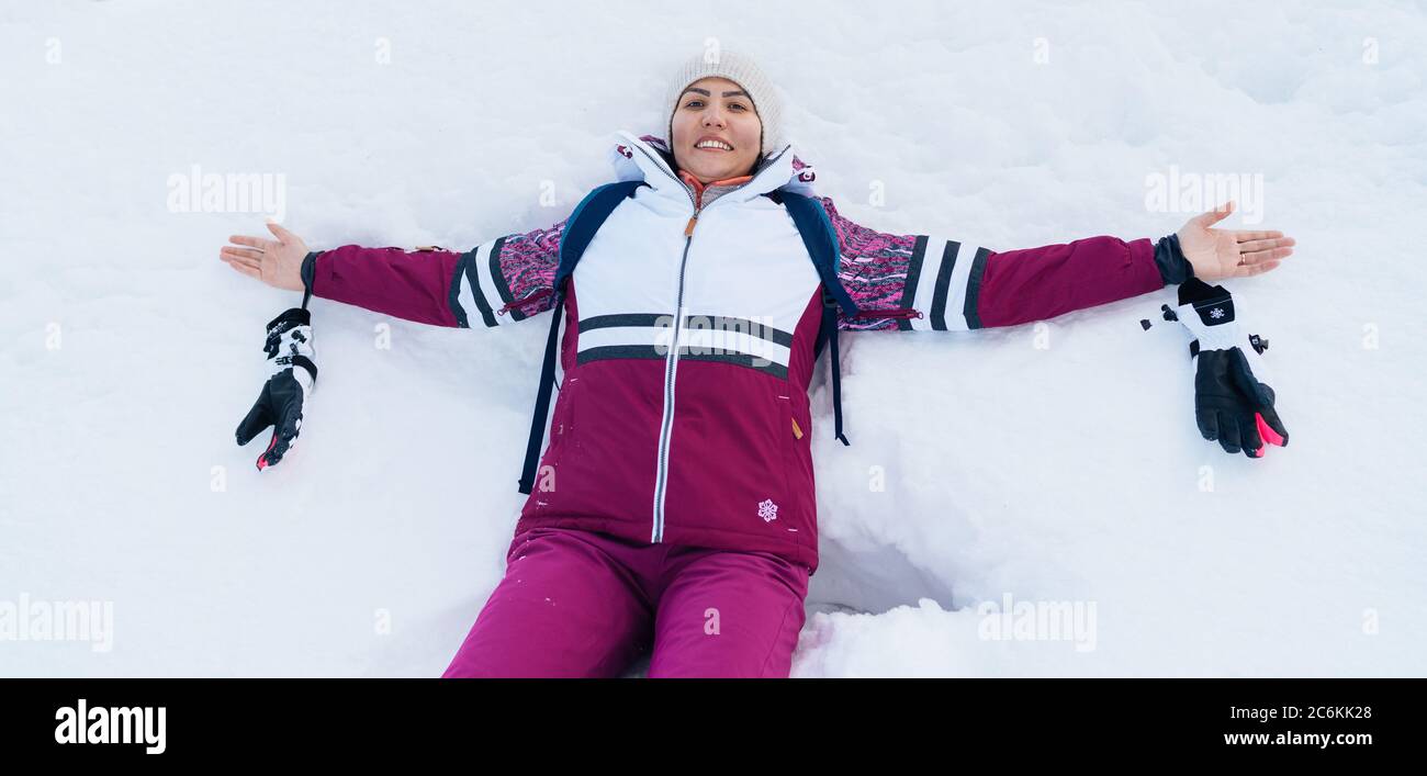 Une jeune femme souriante qui se liait sur la neige blanche ouvrit les bras. Banque D'Images