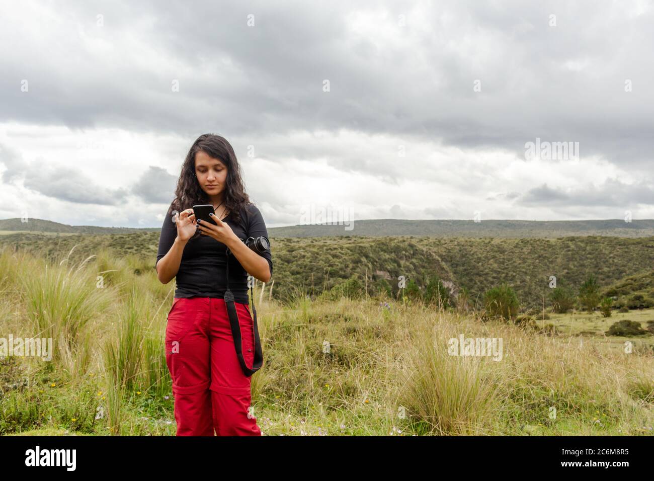 Femme vérifiant son téléphone cellulaire sur une montagne avec une caméra sur son bras Banque D'Images