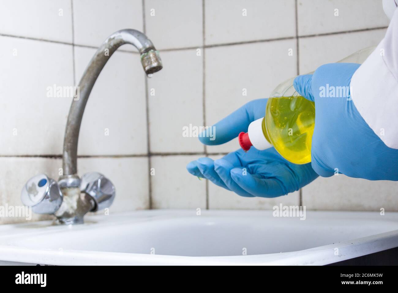 mains dans des gants bleus verser le produit de nettoyage jaune d'une bouteille sur l'évier Banque D'Images