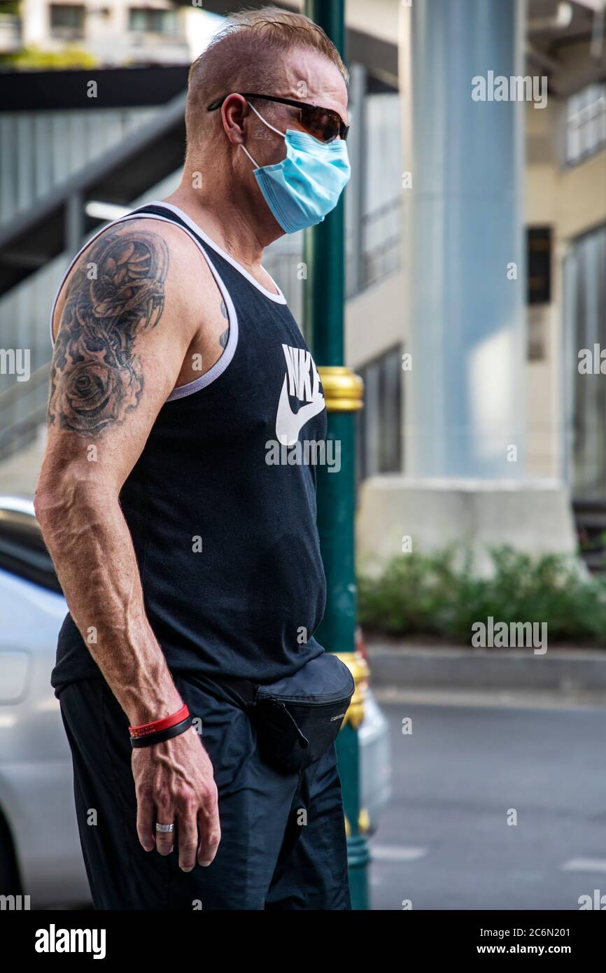 Homme caucasien portant un masque facial et tatouage dans la rue pendant la pandémie de Covid 19, Sukhumvit, Bangkok, Thaïlande Banque D'Images