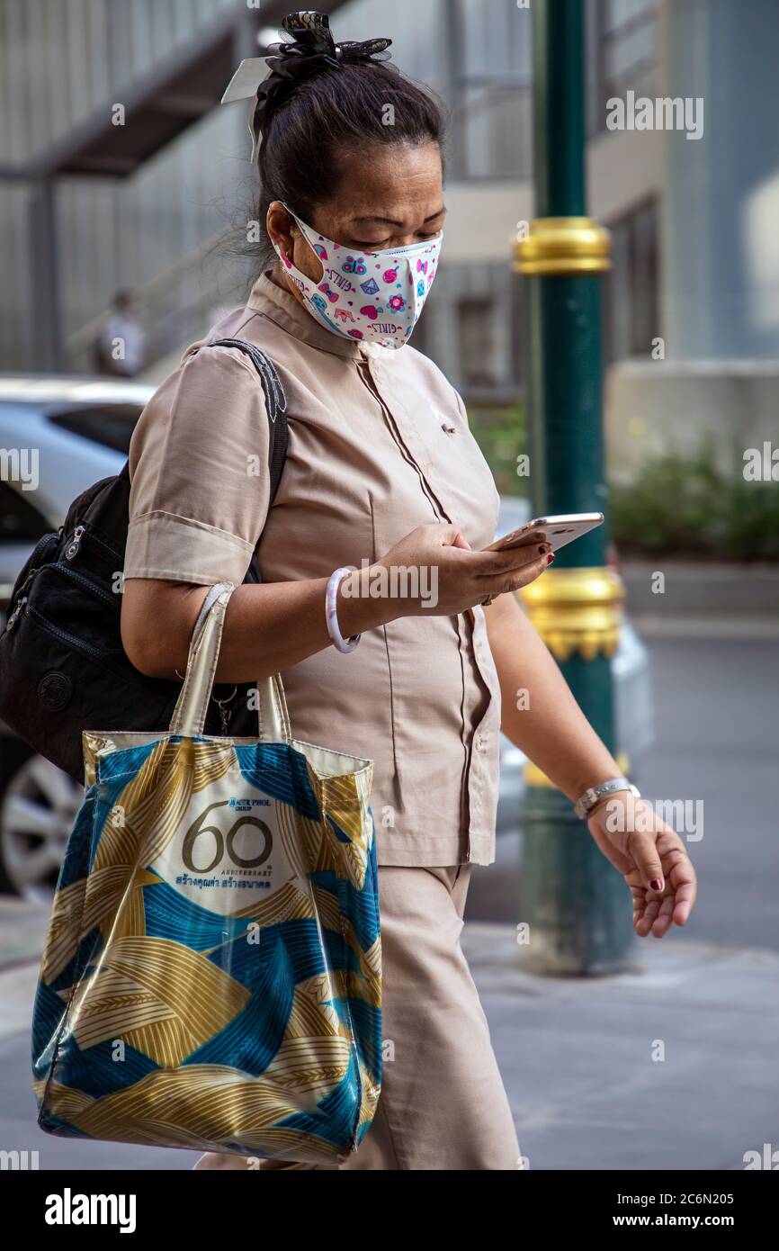 Femme portant un masque facial utilisant un téléphone portable pendant la pandémie Covid 19, Sukhumvit, Bangkok, Thaïlande Banque D'Images