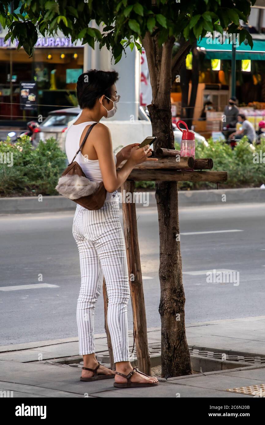 Femme portant un masque facial utilisant un téléphone portable pendant la pandémie Covid 19, Sukhumvit, Bangkok, Thaïlande Banque D'Images