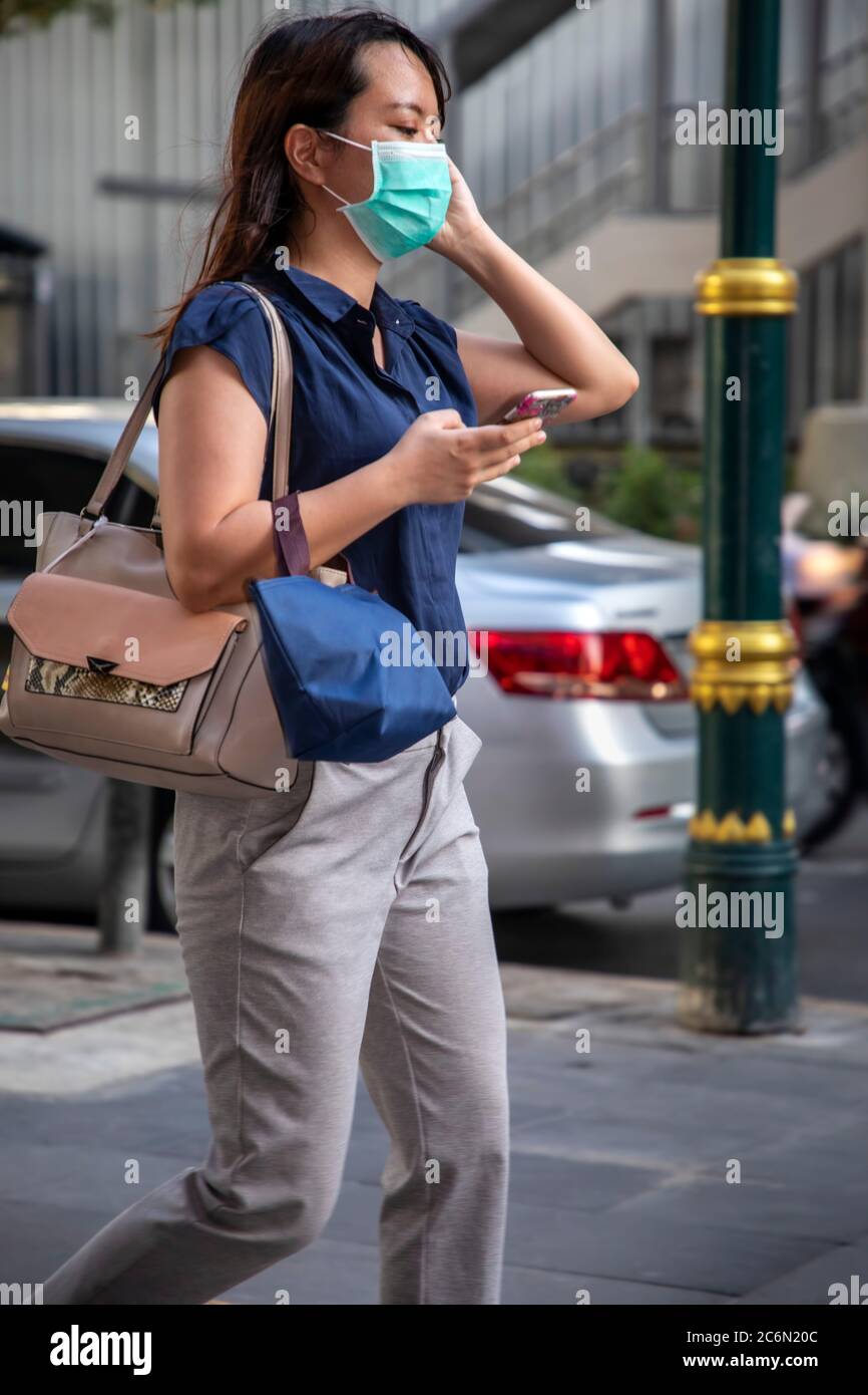 Femme portant un masque facial utilisant un téléphone portable pendant la pandémie Covid 19, Sukhumvit, Bangkok, Thaïlande Banque D'Images