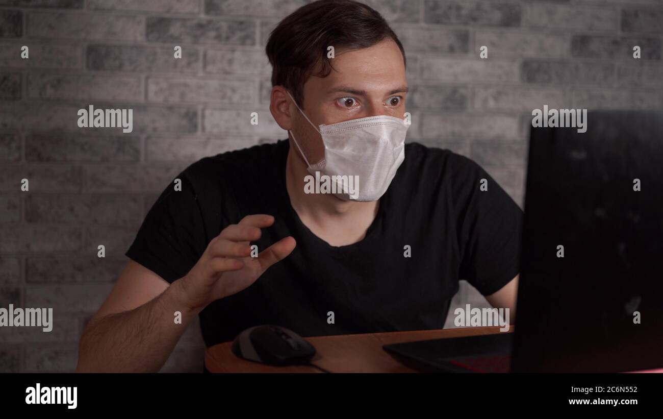 Un homme dans un masque médical apprend des nouvelles sur le coronavirus de l'Internet à l'aide d'un ordinateur portable. L'homme est préoccupé par sa santé. L'épidémie de Banque D'Images