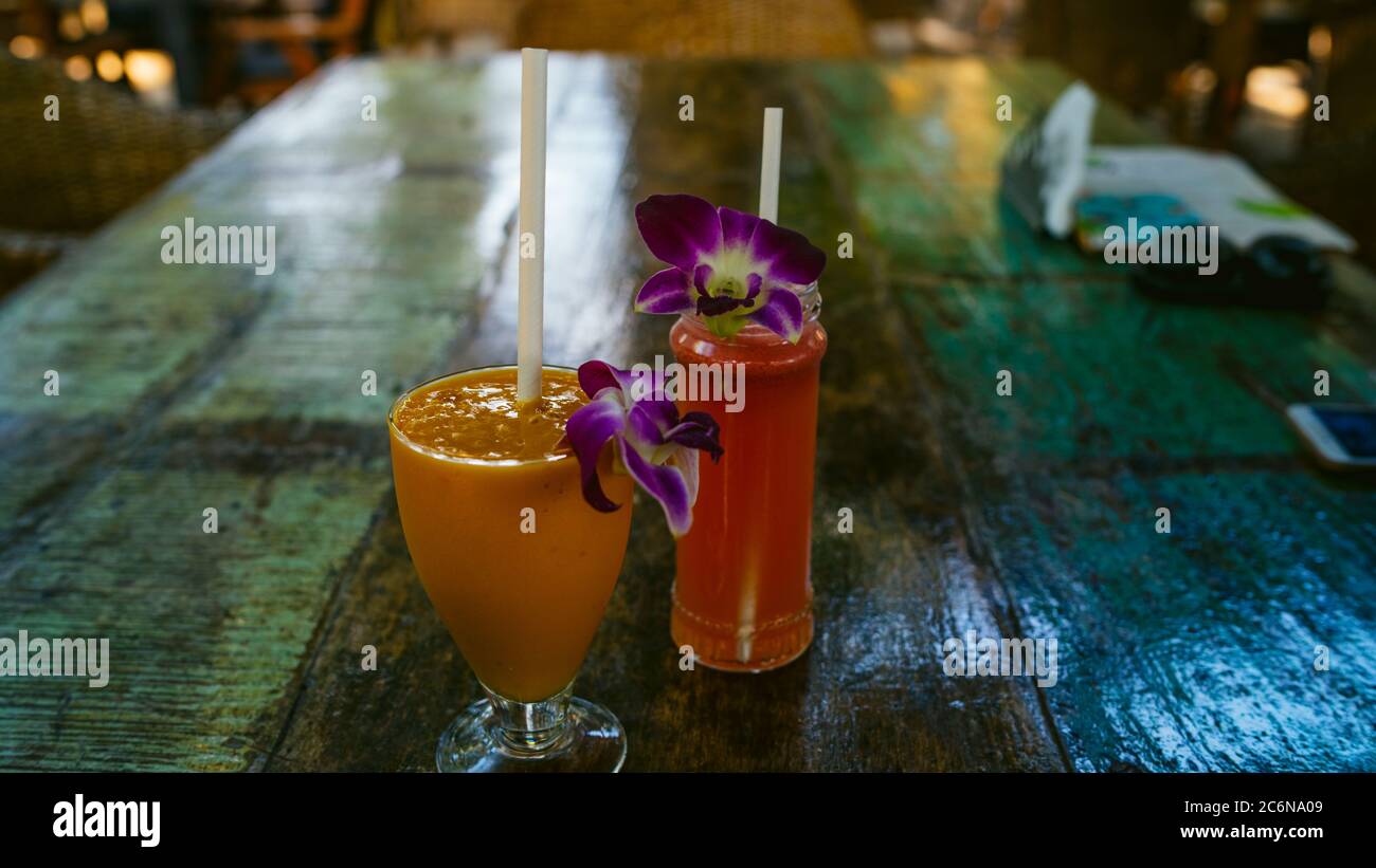 Verre d'orange sur une table en bois dans le café. Savoureuse boisson à l'orange décorée de fleurs dans des verres avec de la paille sur une table en bois dans un café extérieur Banque D'Images