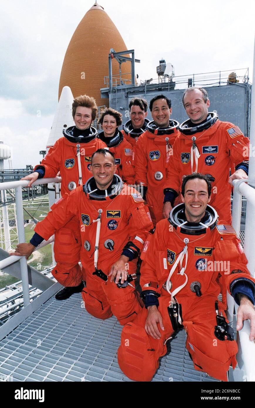 1997 - portant leurs espaces orange de lancement et d'entrée, les membres de l'équipage STS-84 sont tous souriants alors qu'ils posent pour une photo de groupe au Launch Pad 39A avec la navette spatiale Atlantis en arrière-plan. Les spécialistes de mission Jean-François Clervely, à droite, de l'Agence spatiale européenne, et Carlos I. Noriega sont à genoux devant nous. Debout, de gauche à droite, se trouvent Elena V. Kondakova, spécialiste de mission de l'Agence spatiale russe, Eileen Marie Collins, C. Michael Foale et Edward Tsang lu, spécialistes de mission, et Charles J. Precourt, commandant de mission. Banque D'Images