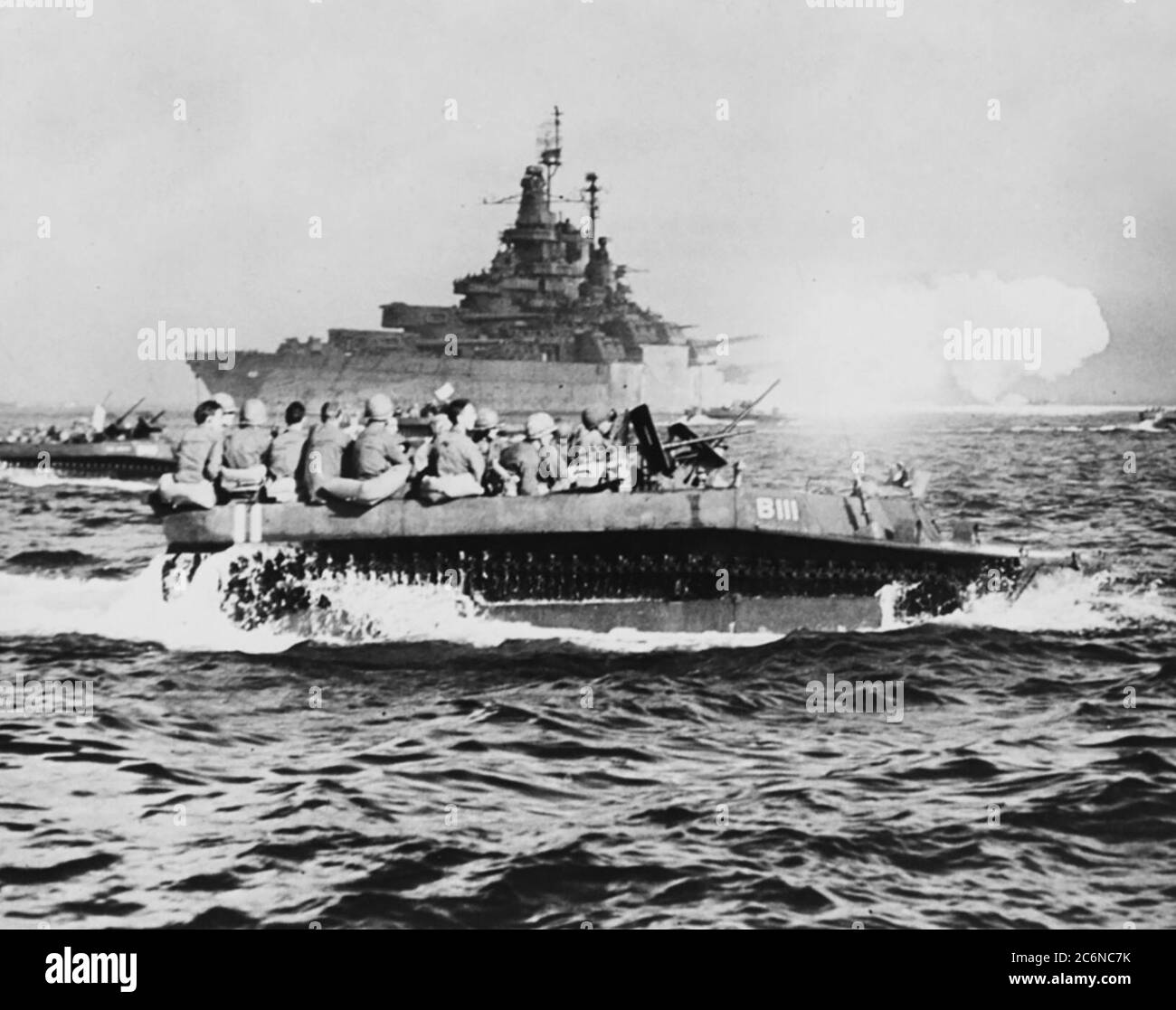 Le USS Tennessee bombarde Okinawa avec ses 14/50 canons à batterie principaux le 1er avril 1945, tandis que les véhicules d'atterrissage sur chenilles transportent des troupes sur les plages d'invasion Banque D'Images