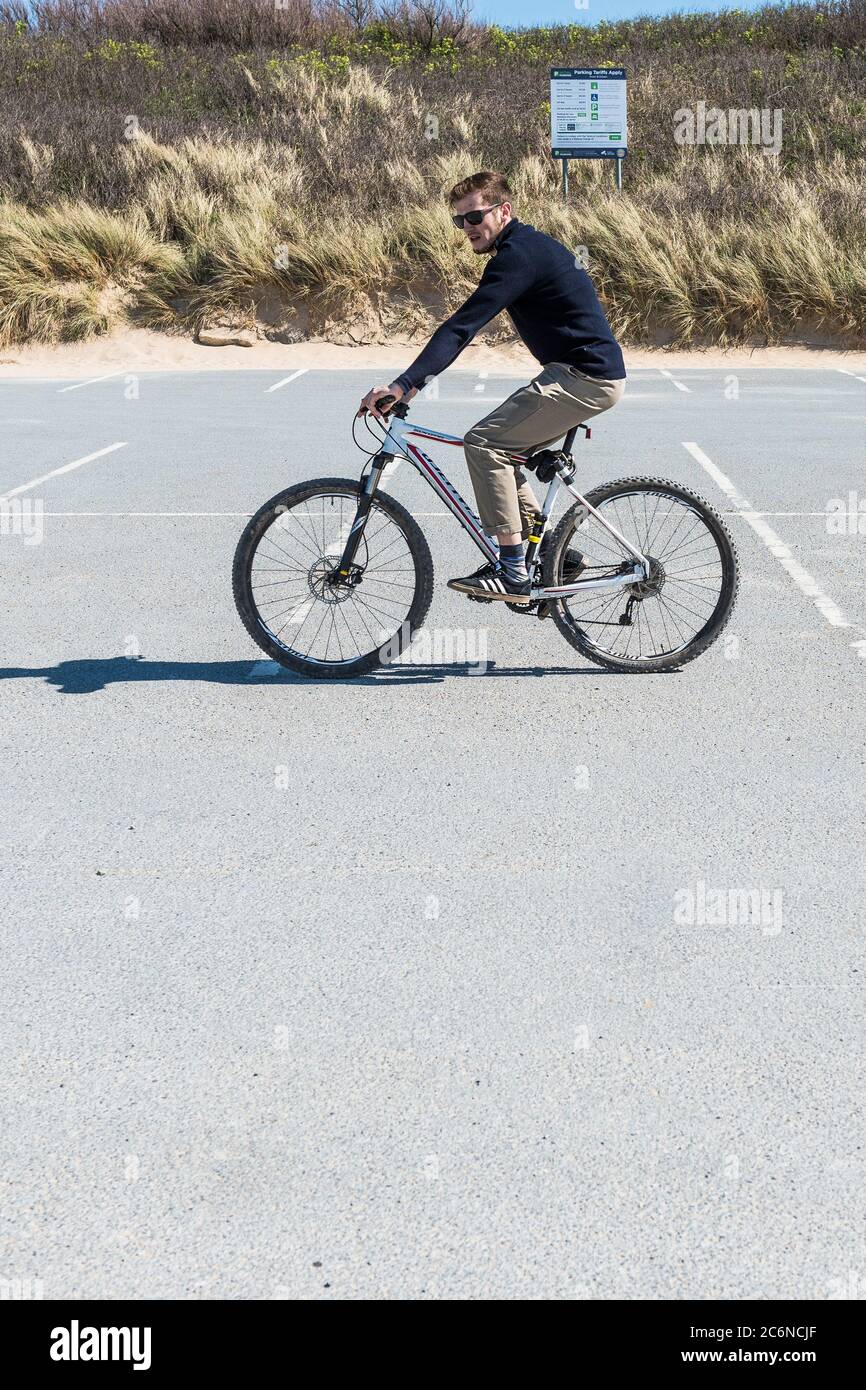 Un homme qui monte un vélo à travers un parking vide et déserté à Fistral à Newquay, en Cornwall. Banque D'Images